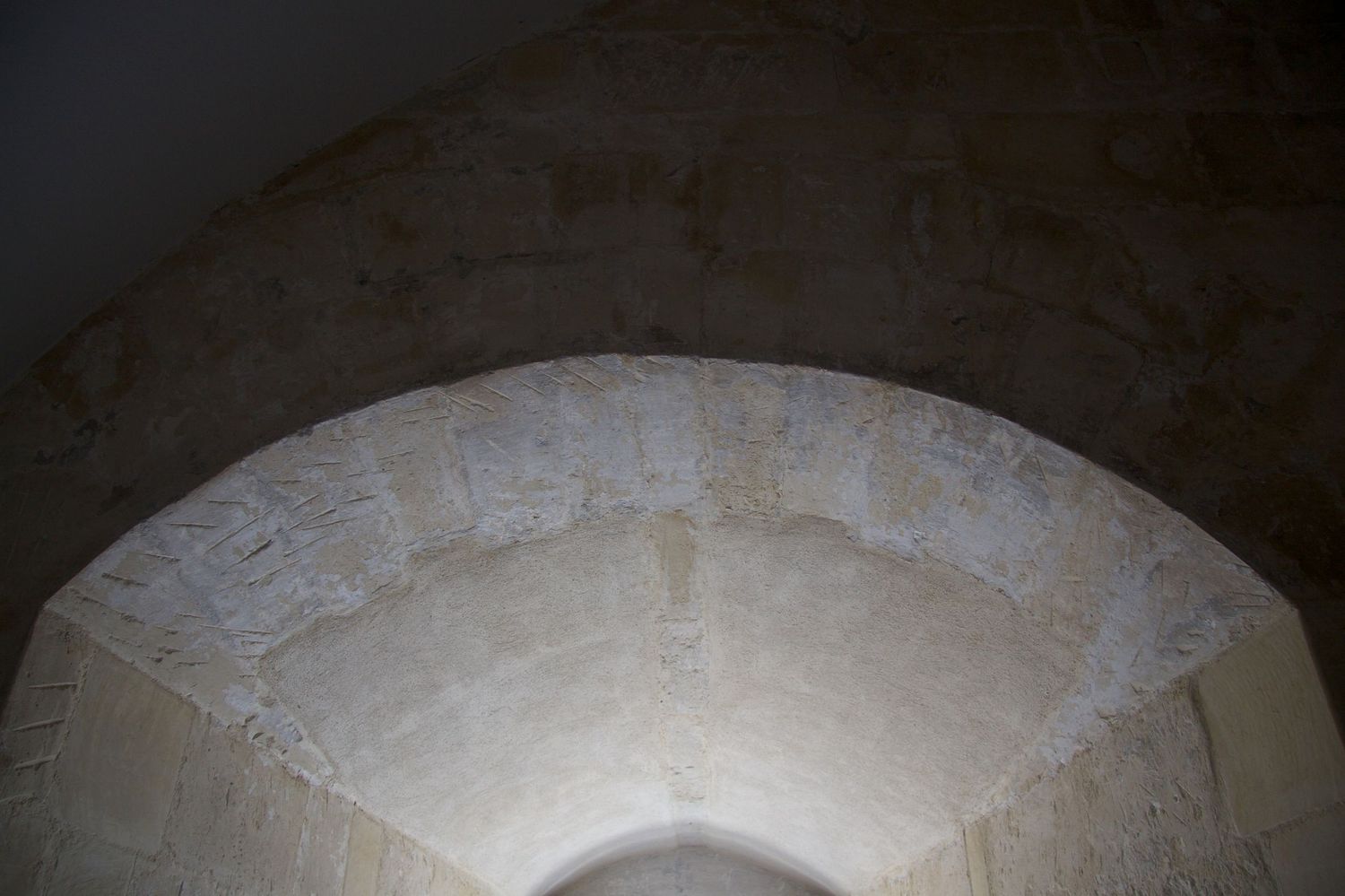 Close-up of a weathered stone arch ceiling with rough limestone texture in an ancient historic building interior.