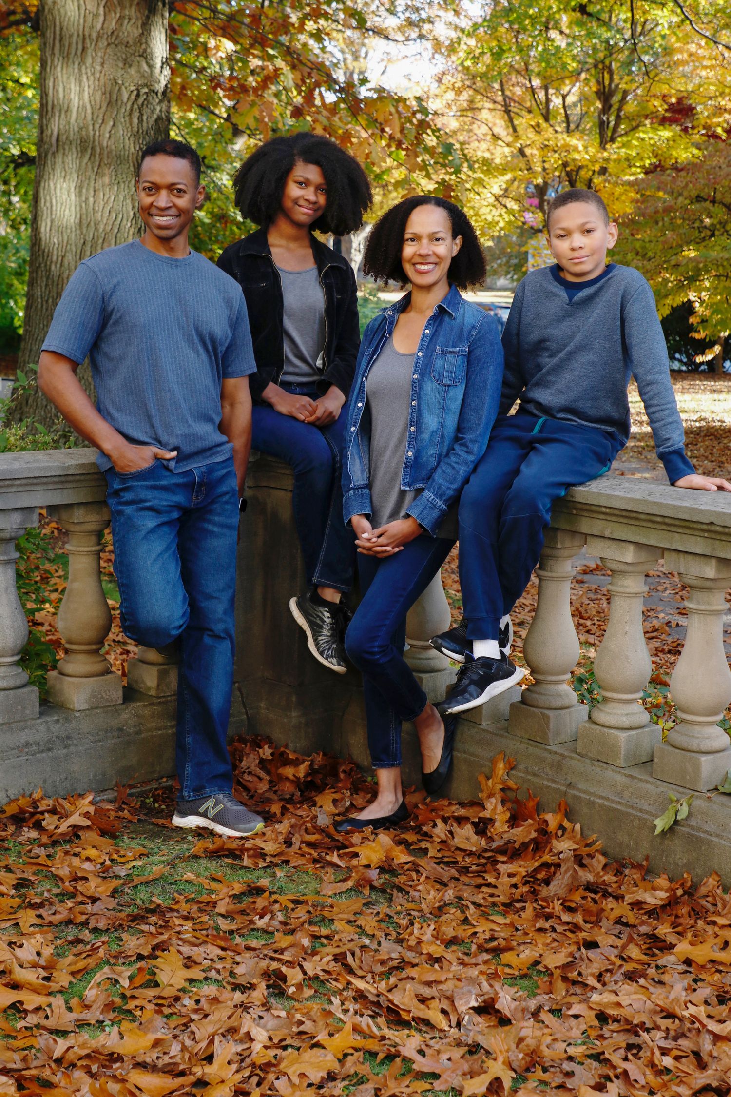 Happy family of four posing outdoors among colorful autumn foliage and fallen leaves.