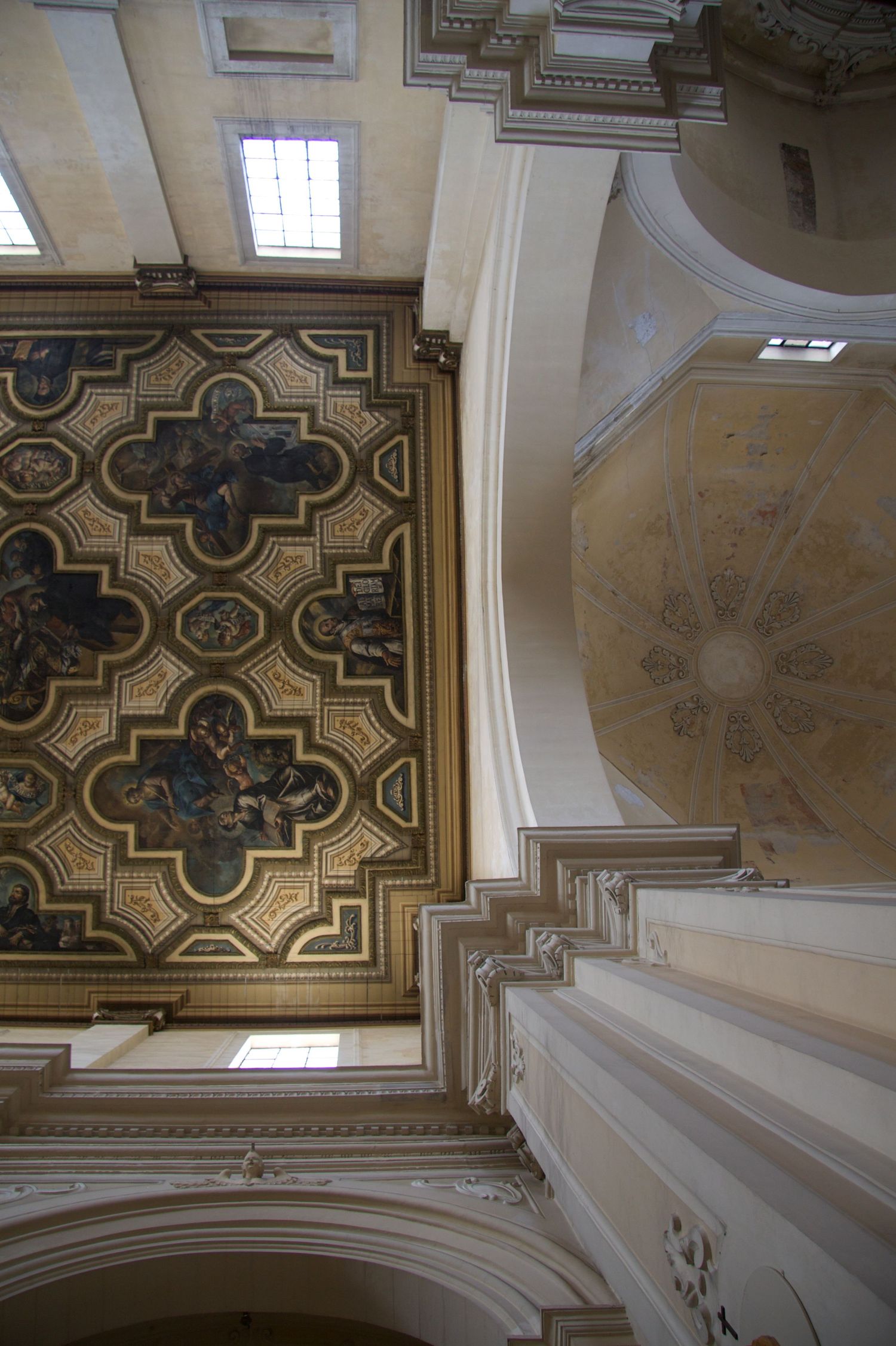 Ornate painted ceiling of a Baroque church featuring gold geometric patterns and religious frescoes with arched dome architecture.