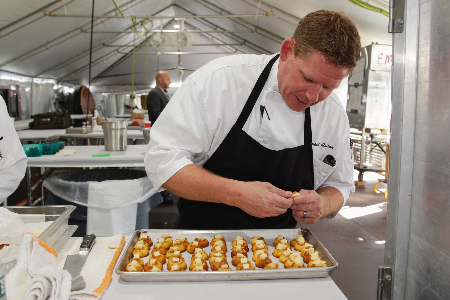 Professional chef carefully garnishes a tray of elegant appetizers in a catering kitchen tent.