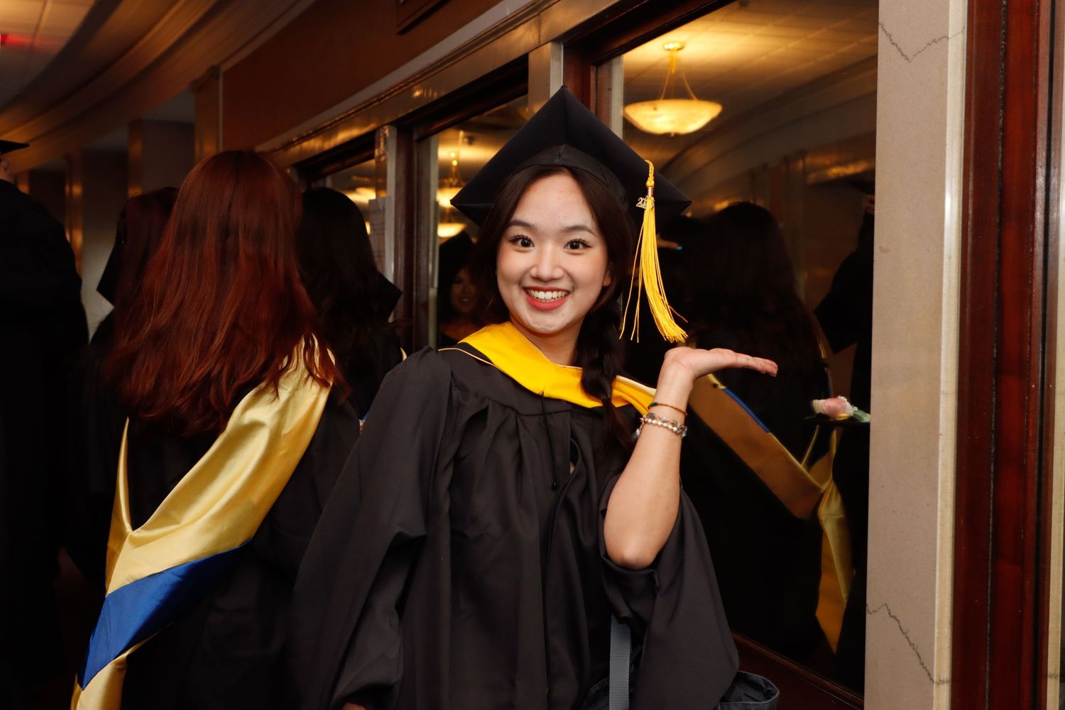 Smiling graduate in black and gold cap and gown posing at graduation ceremony.