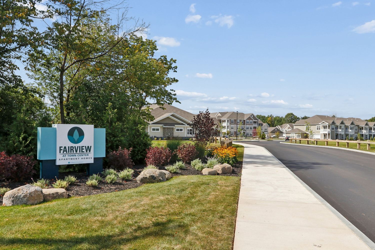 Fairview apartment community entrance sign surrounded by colorful landscaping and manicured gardens along a paved driveway.