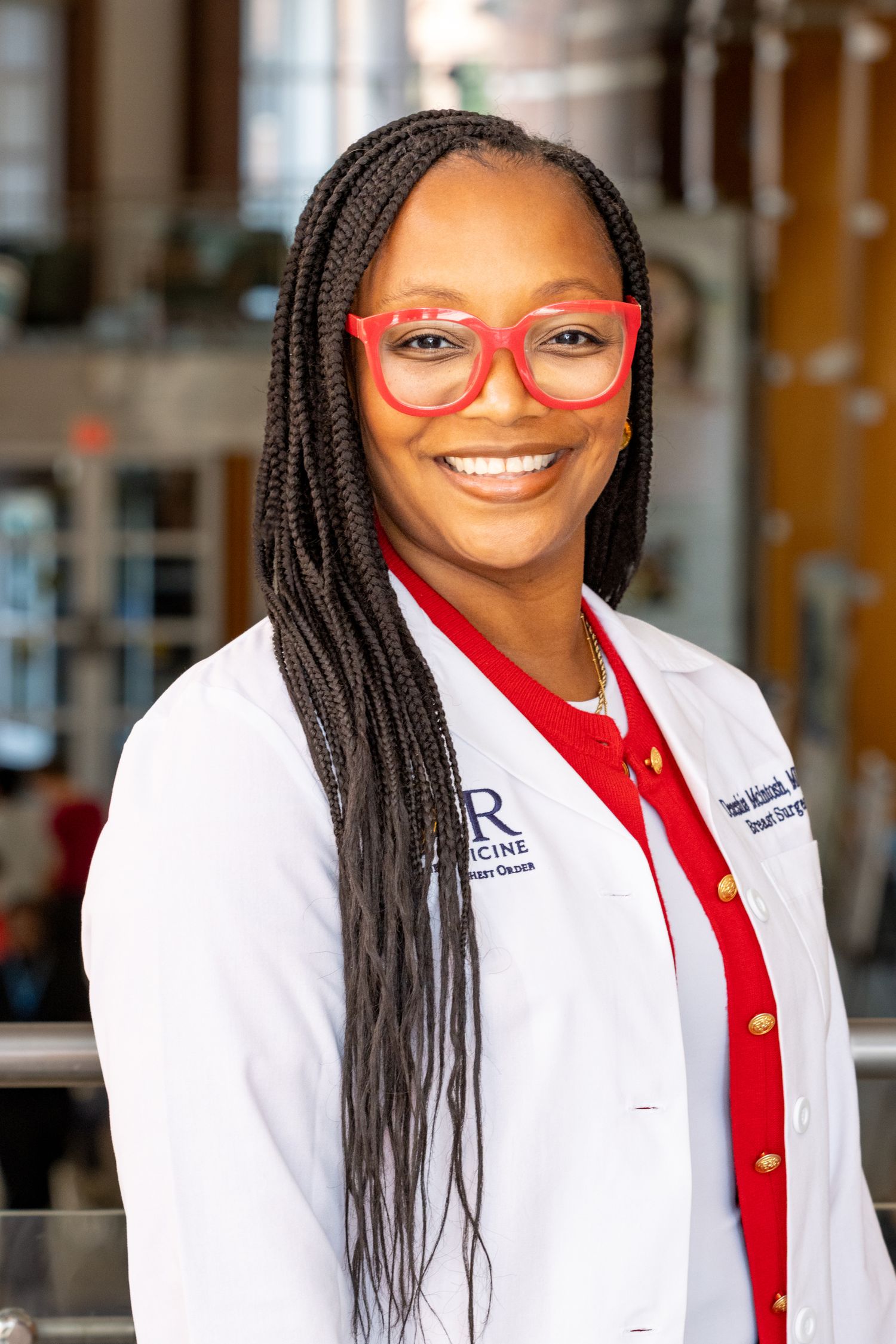 Female doctor in white UR Medicine coat and red glasses smiling outdoors.