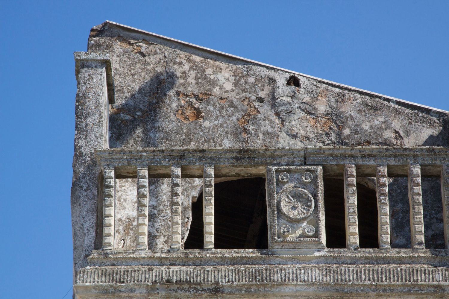Ancient stone building facade with decorative carved details and circular medallion under blue sky.