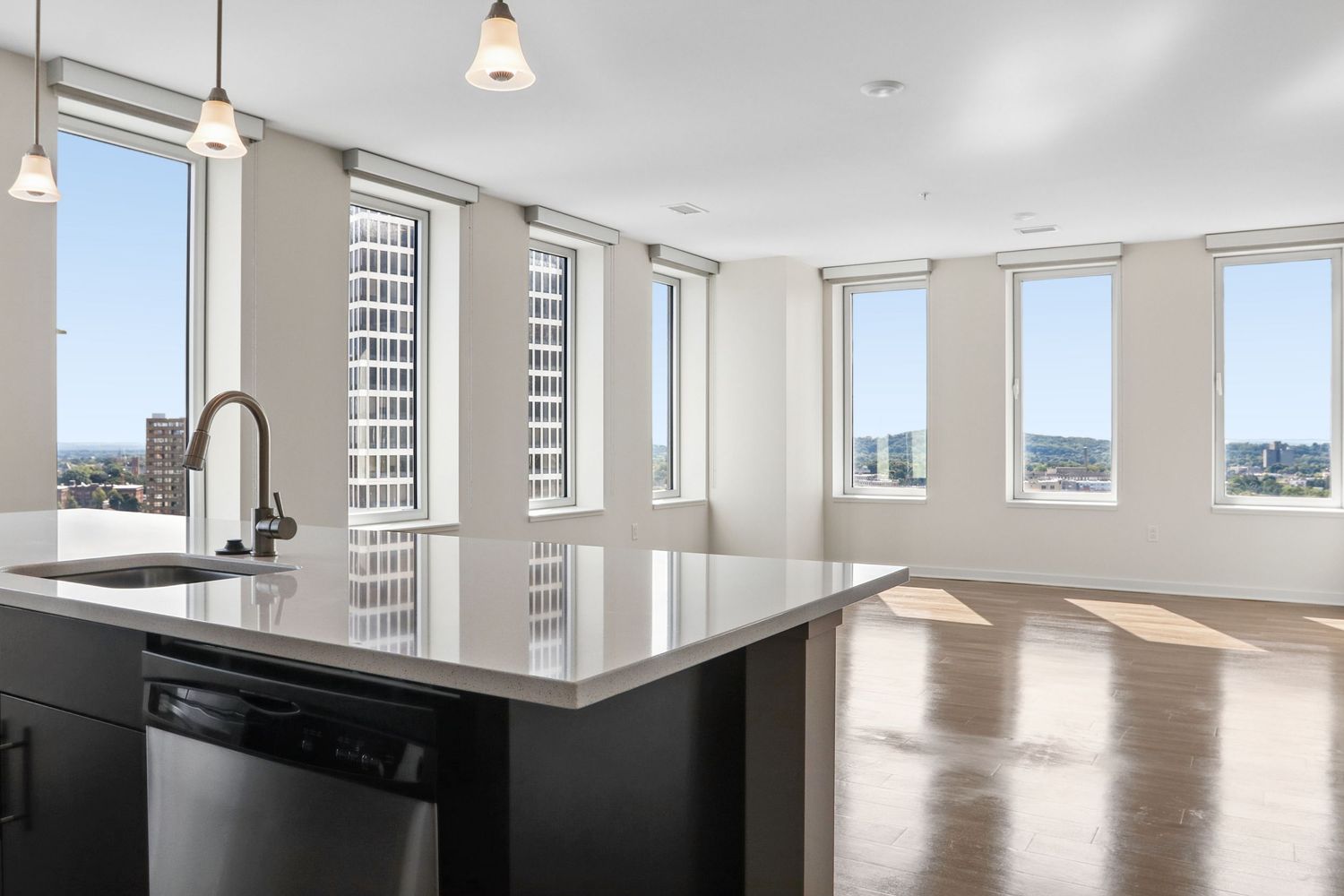 Spacious high-rise apartment kitchen with dark island, black countertops, and floor-to-ceiling windows with city views.