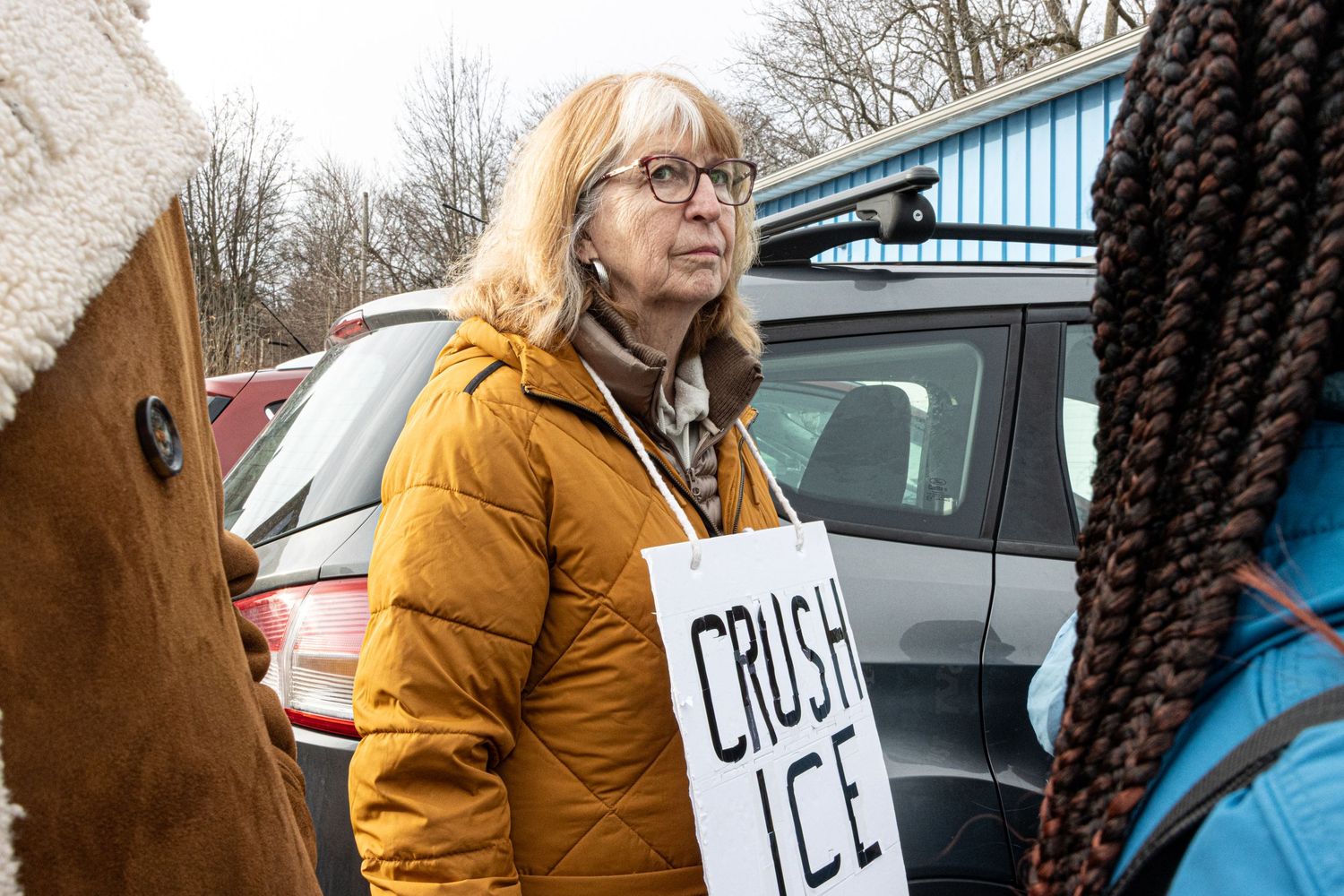 Woman in yellow jacket holding a Crush ICE protest sign at an outdoor demonstration.