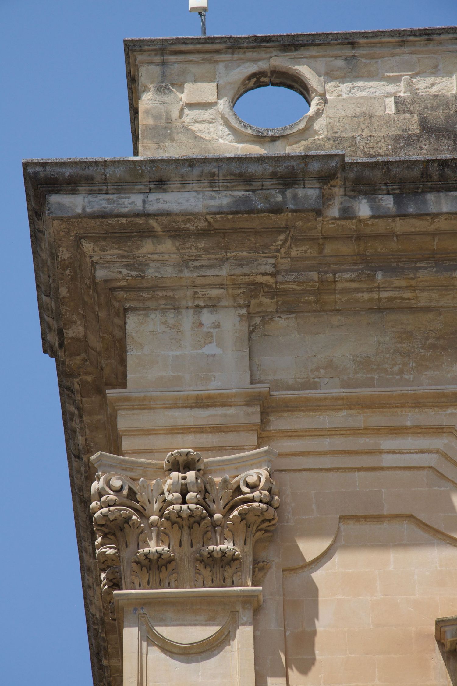 Decorative stone capital with floral motifs on a historic building corner against blue sky.
