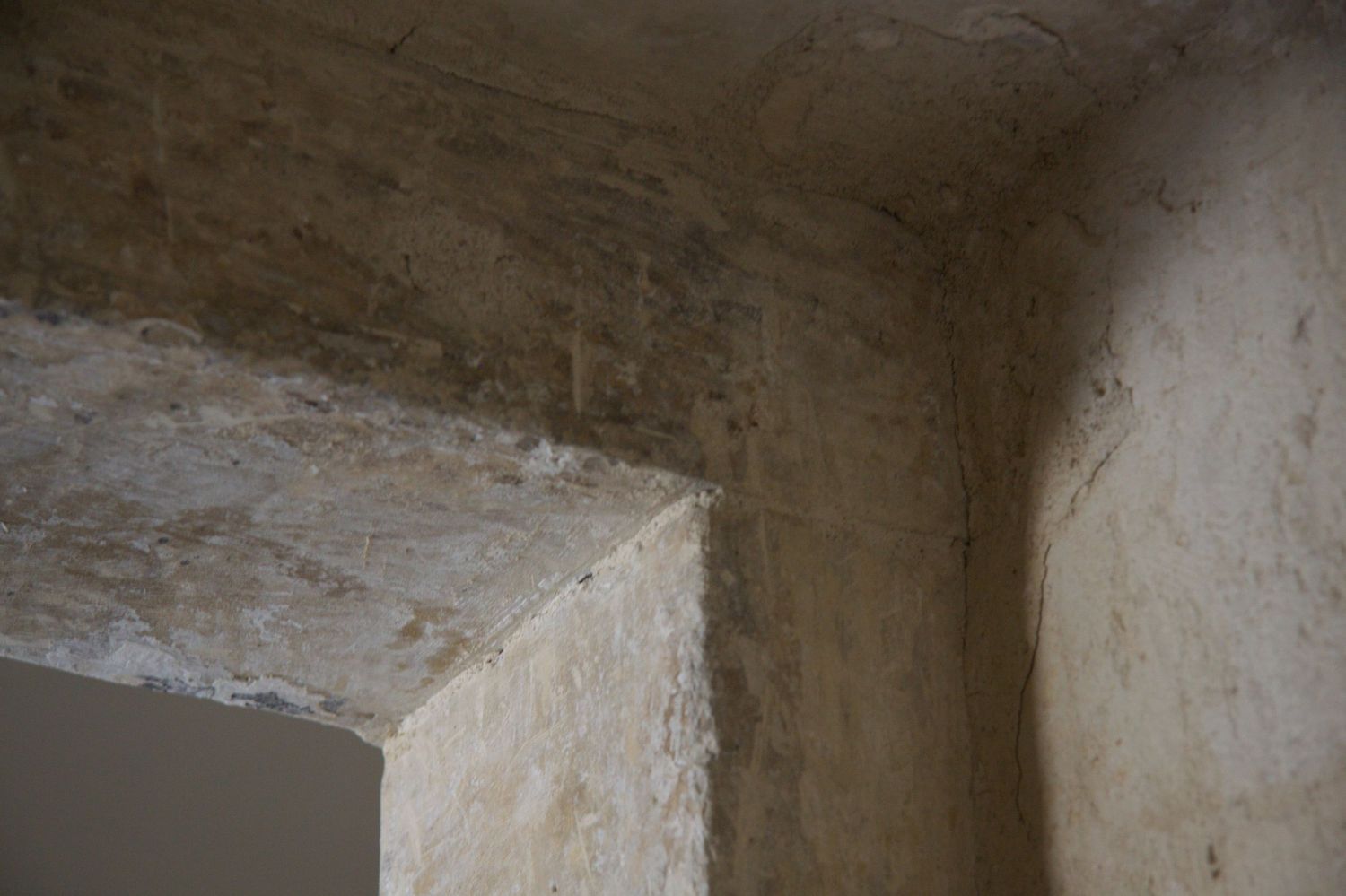 Interior corner of an aged stone room with rough plastered walls and ceiling.