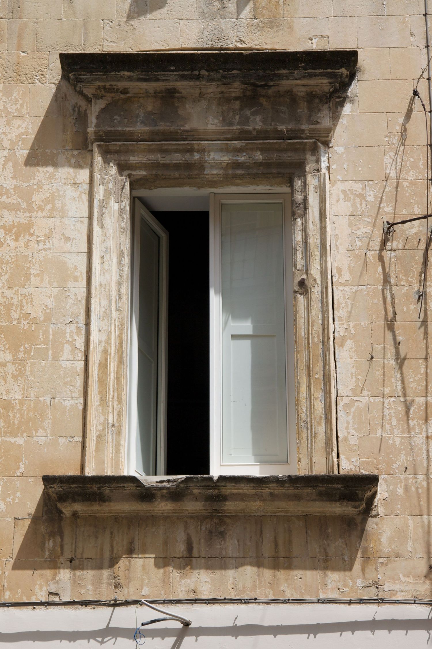 Weathered limestone building facade with open white casement window and decorative stone molding surround.