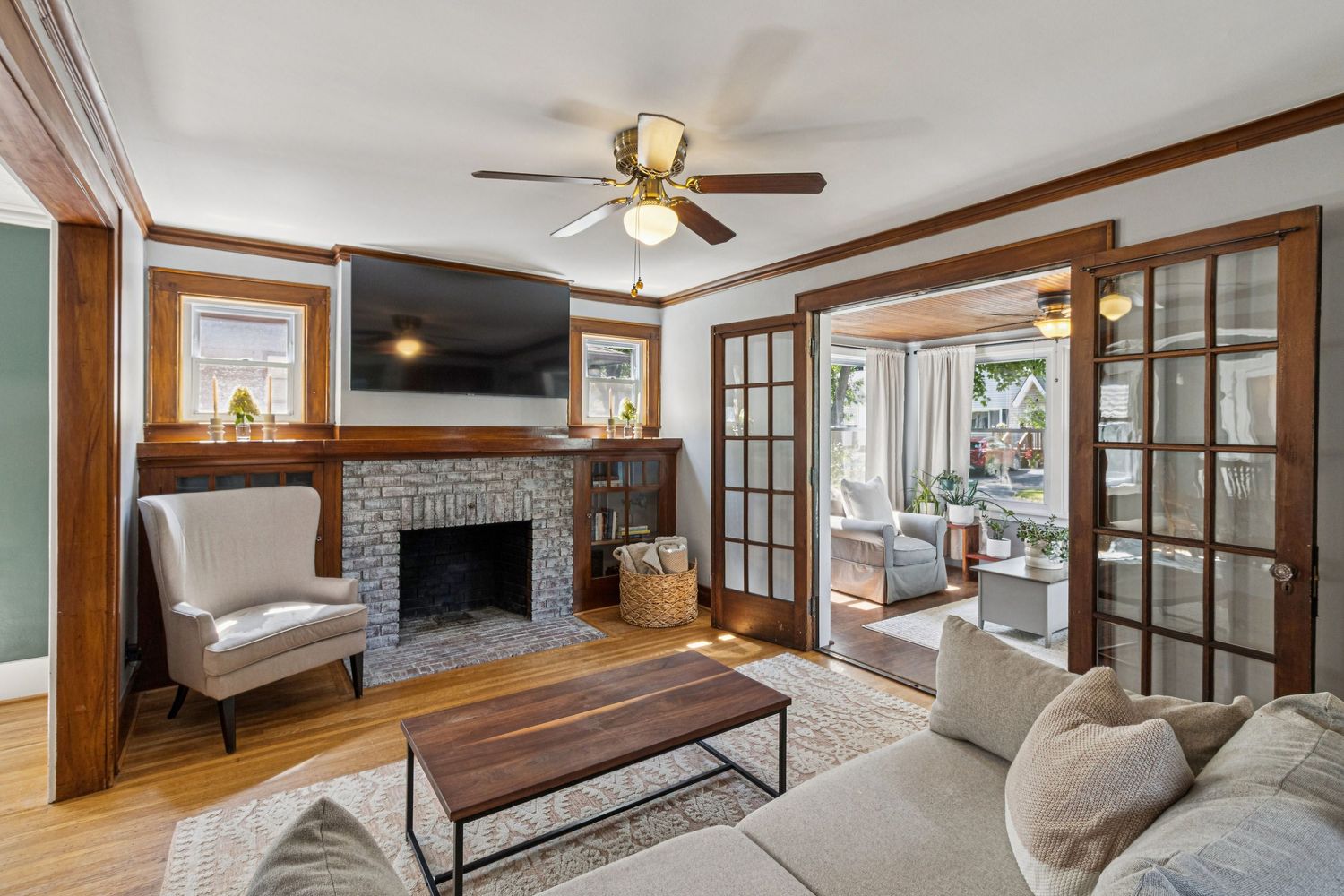 Cozy living room with stone fireplace, hardwood floors, ceiling fan, and French doors leading to sunroom.