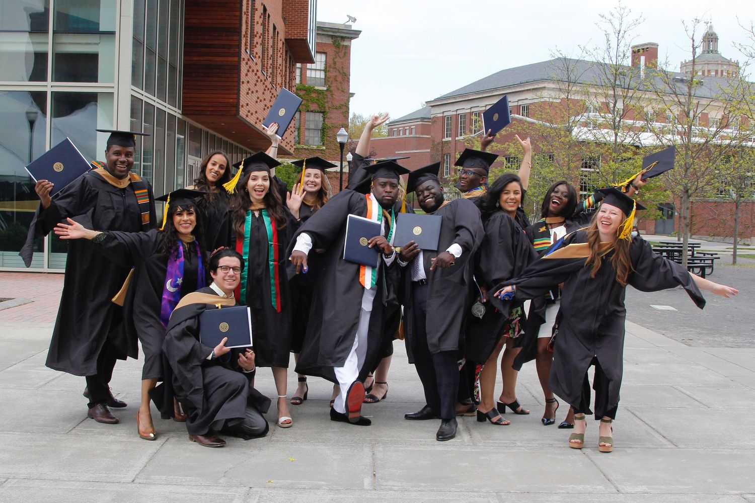 Excited graduates in black caps and gowns celebrating outdoors on a university campus plaza.