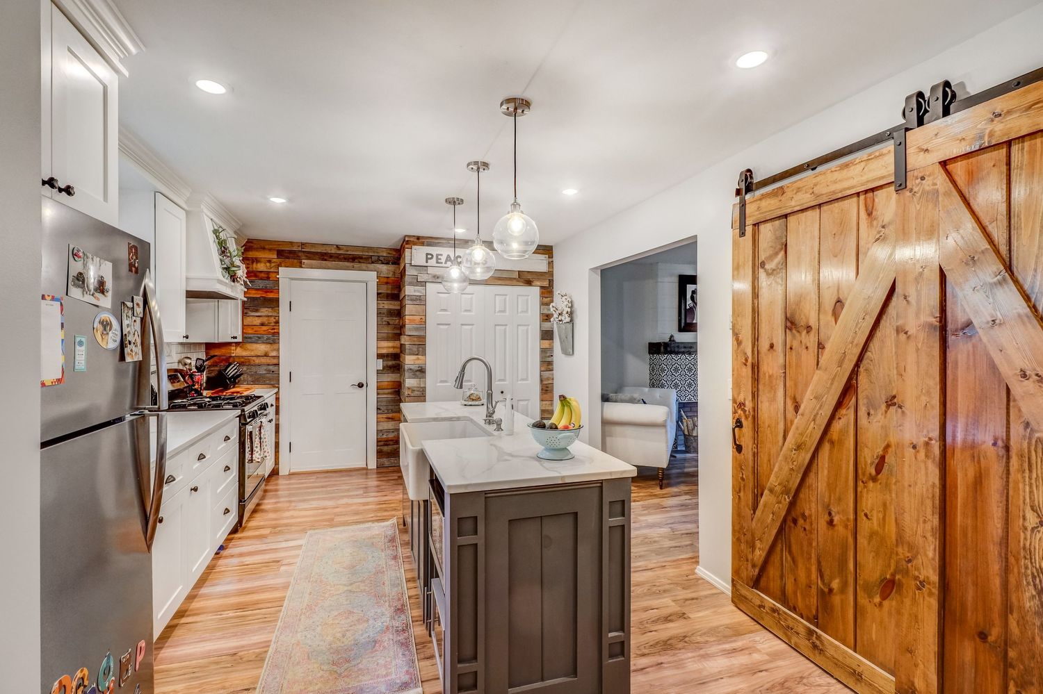 Modern farmhouse kitchen with white cabinets, island, pendant lights, and rustic sliding barn door on hardwood floors.