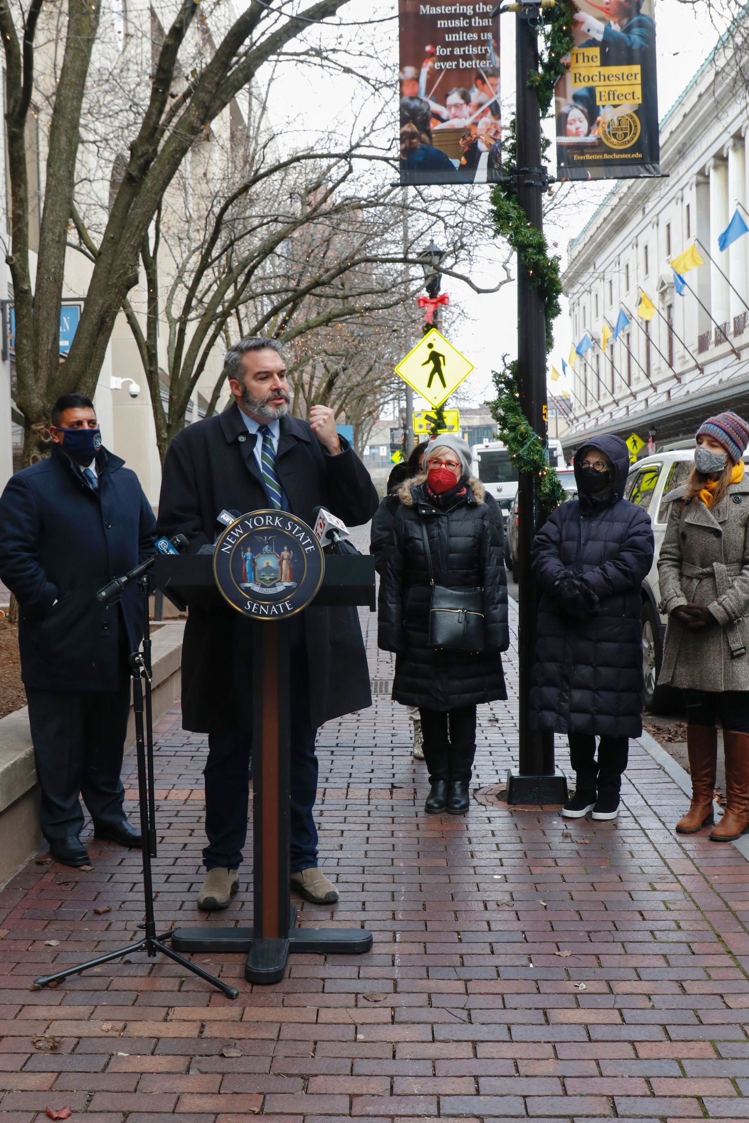 Man speaking at New York State Senate podium outdoors during winter press conference.