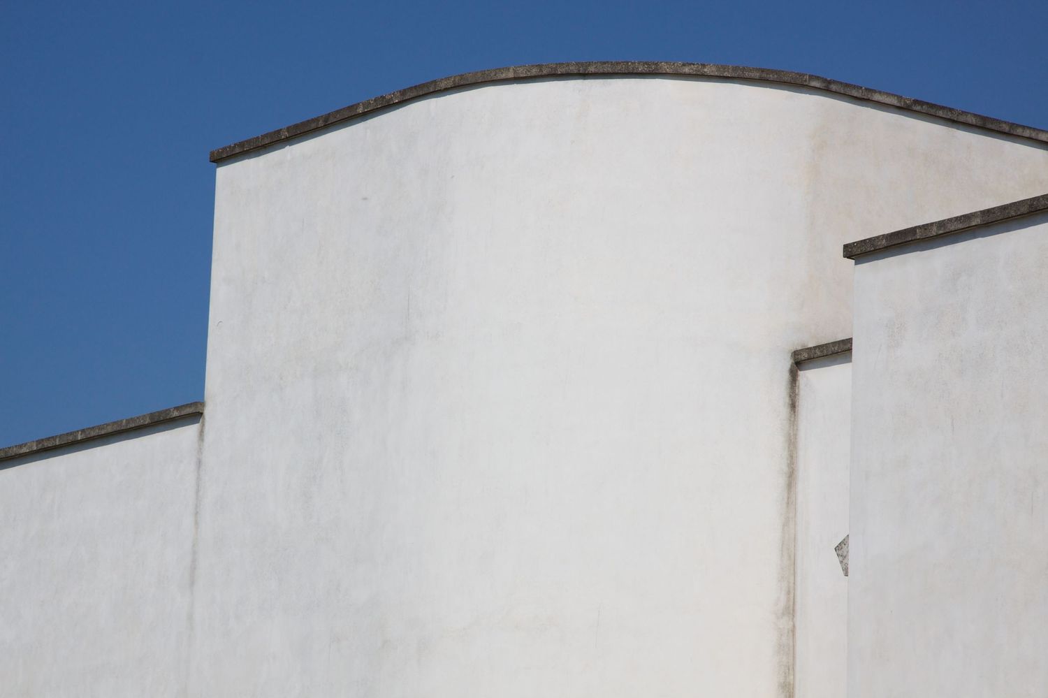 Abstract white curved architectural walls forming geometric shapes against a vivid blue sky.