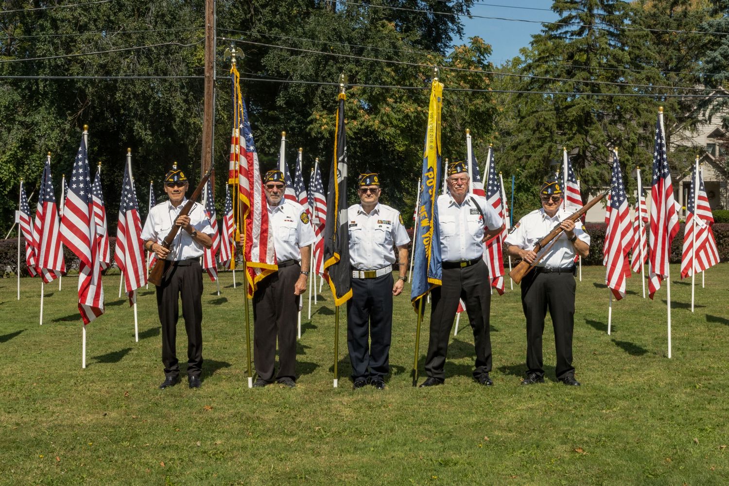 Veterans color guard standing proudly with American flags displayed on sunny outdoor grounds.