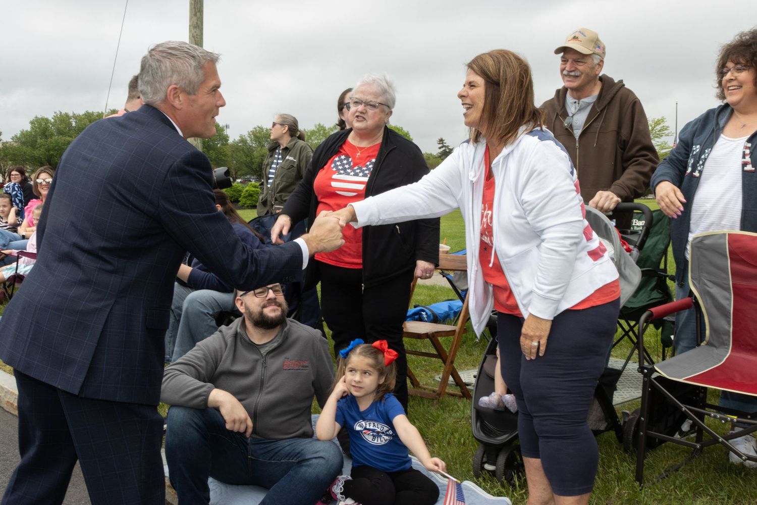 Politician greeting a woman in a white jacket at an outdoor community parade event.