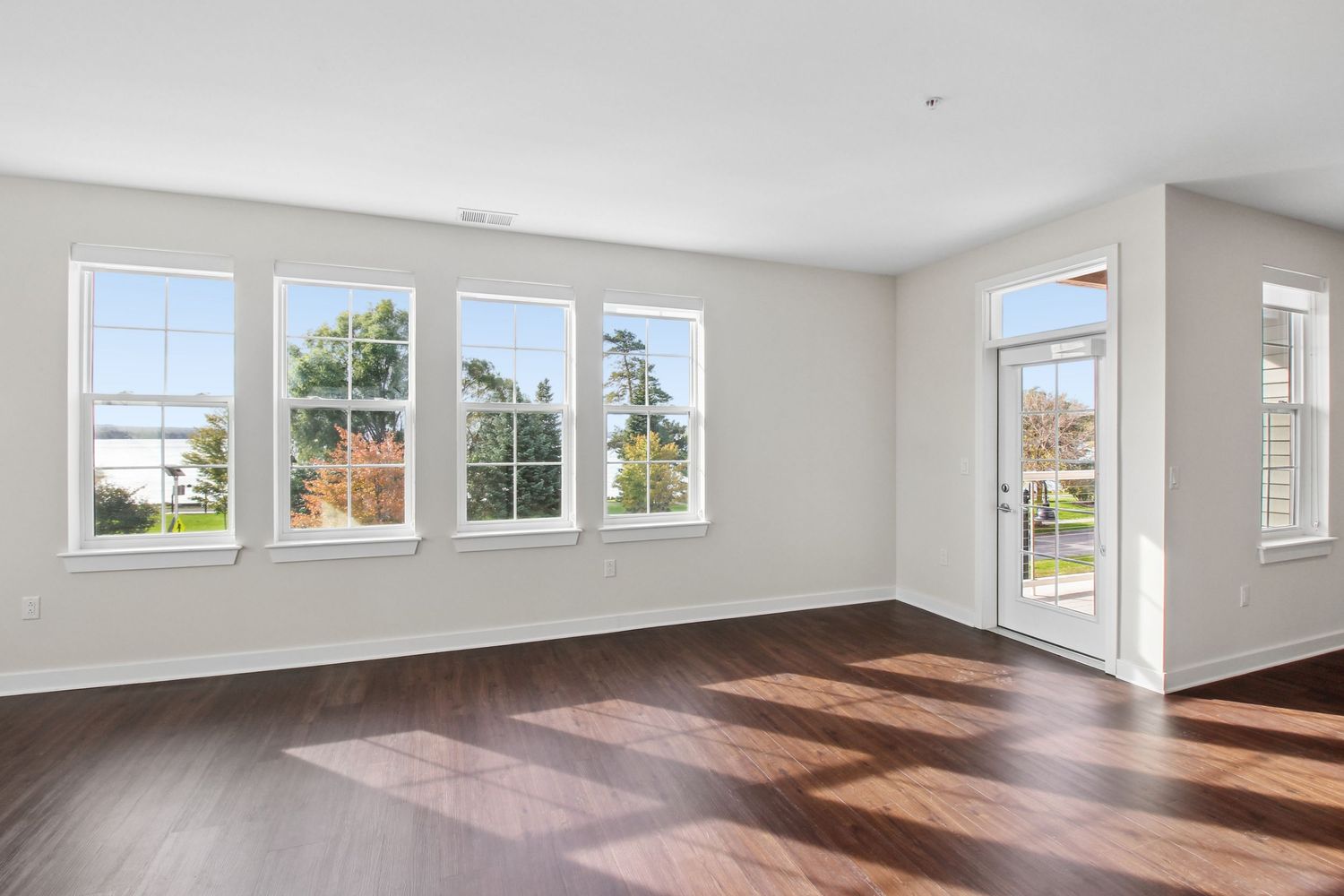 Bright empty apartment living room with hardwood floors, large windows, and a glass door leading to an outdoor balcony.
