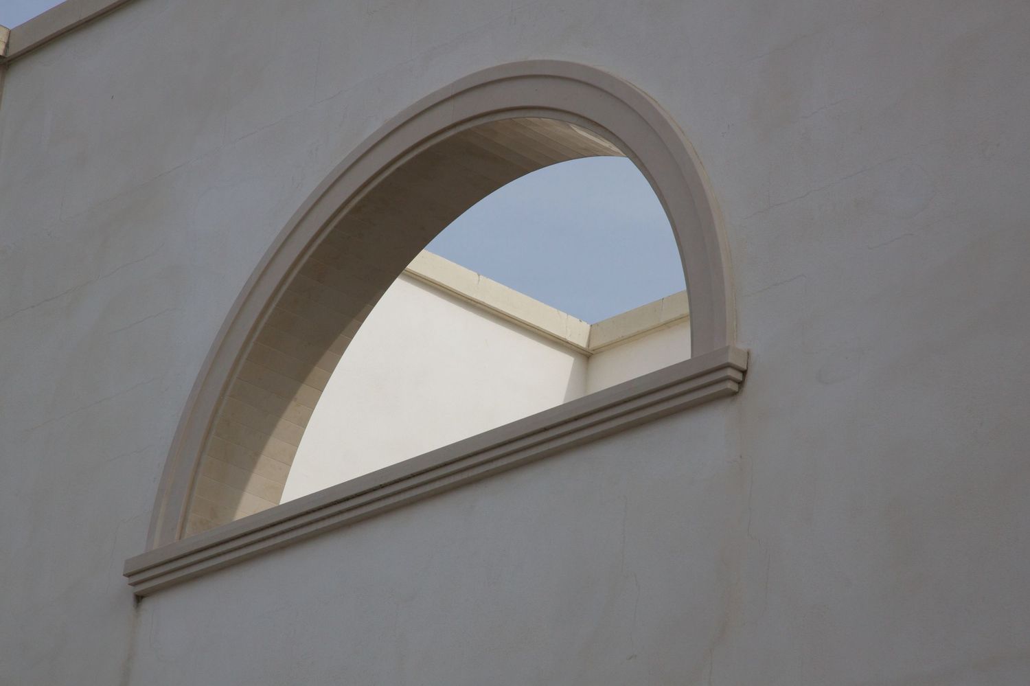 Semi-circular arched window framed in white stucco against a blue sky.