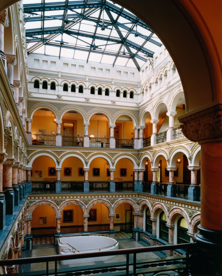 Grand interior atrium with arched colonnades, balconies, and glass skylight ceiling.