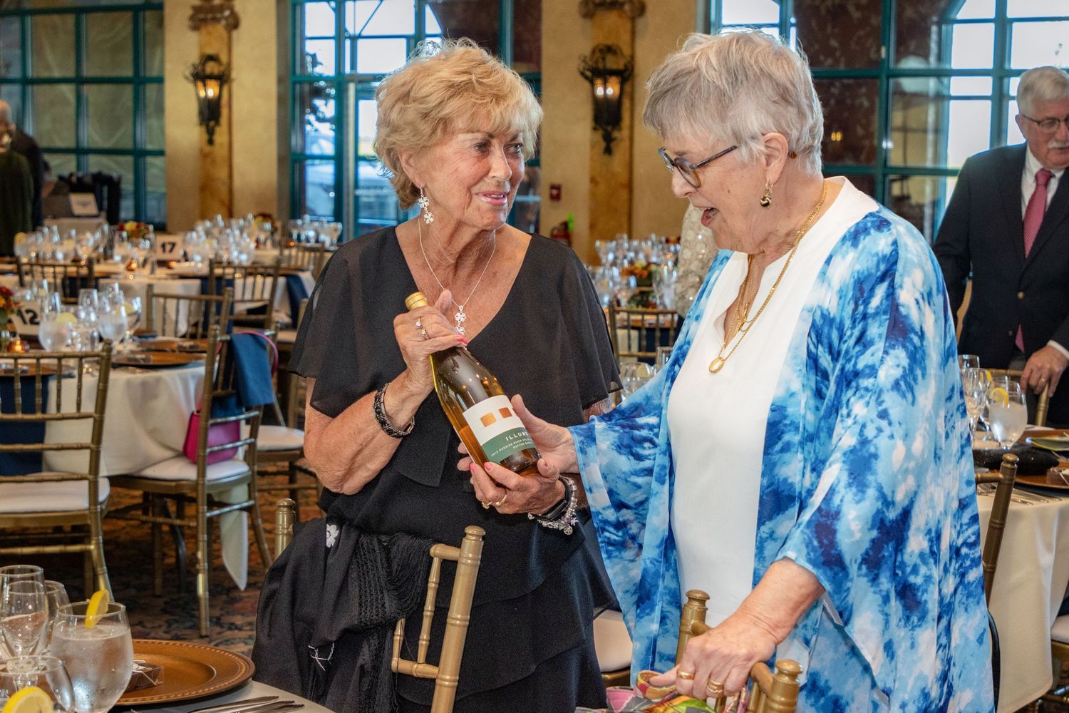 Two women examining a wine bottle at an elegant charity fundraiser dinner event.