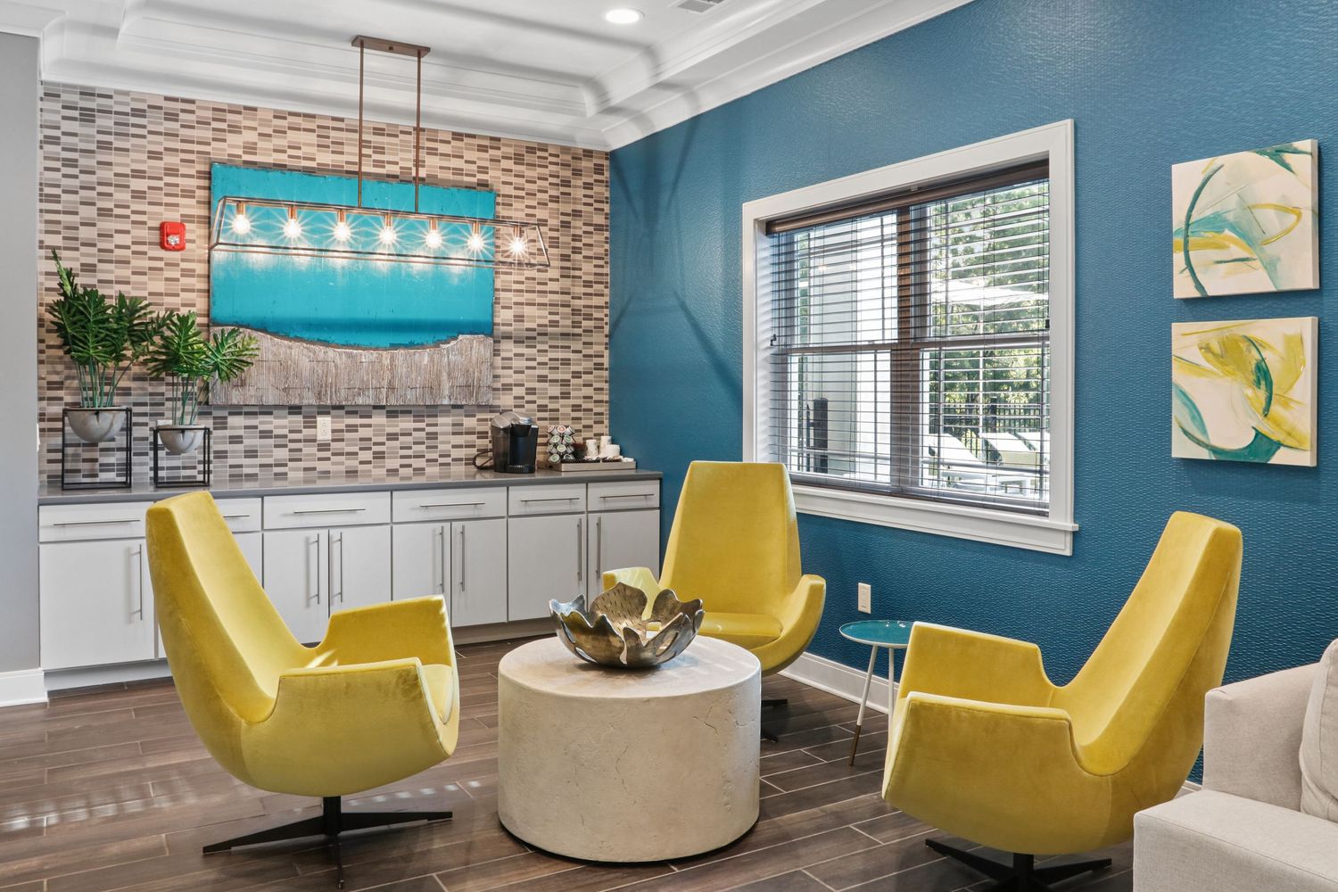 Modern lounge with yellow chairs, round coffee table, teal accent wall, and mosaic tile backsplash.
