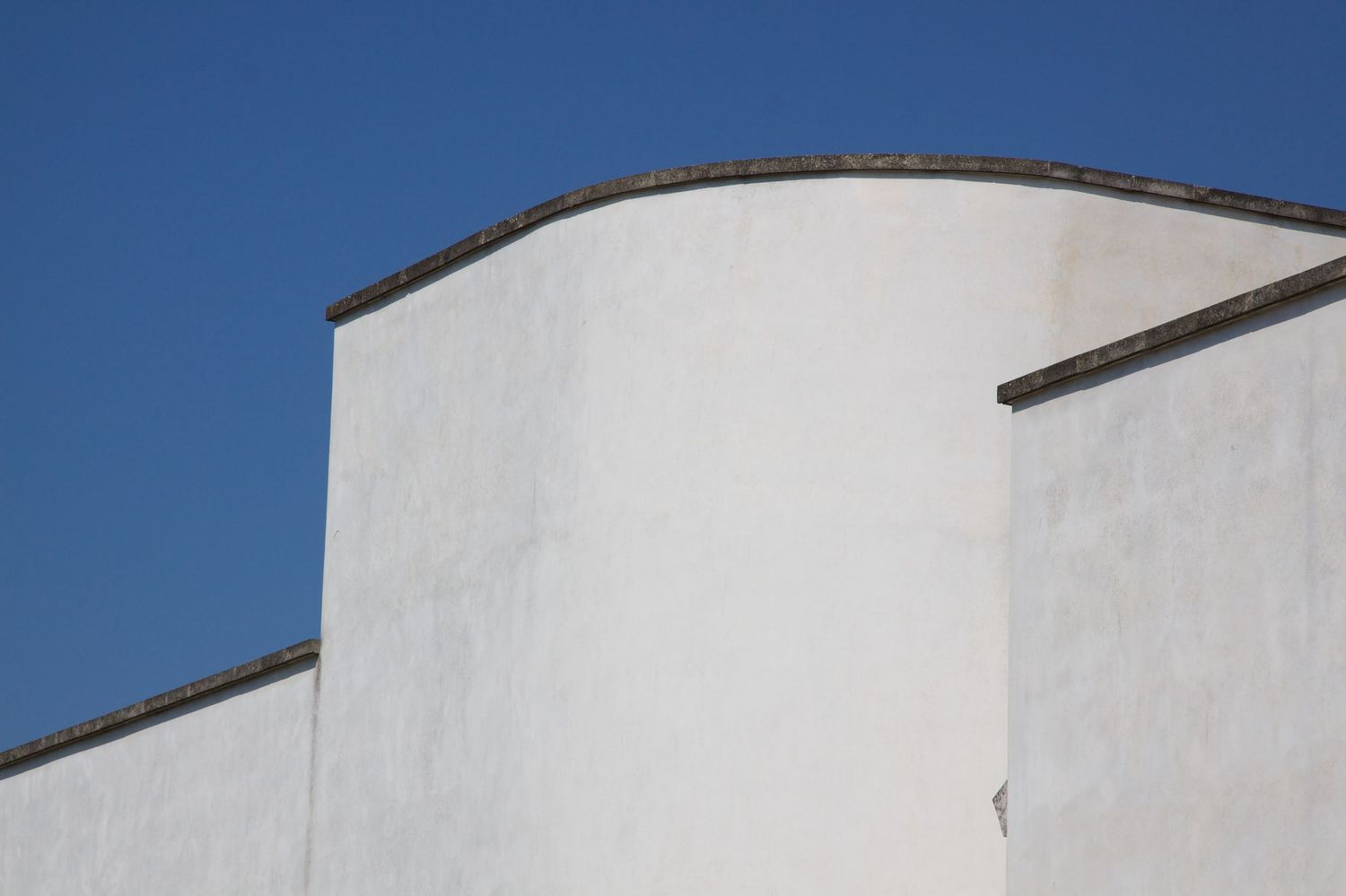 Minimalist white curved building walls with clean geometric shapes against a bright blue sky.