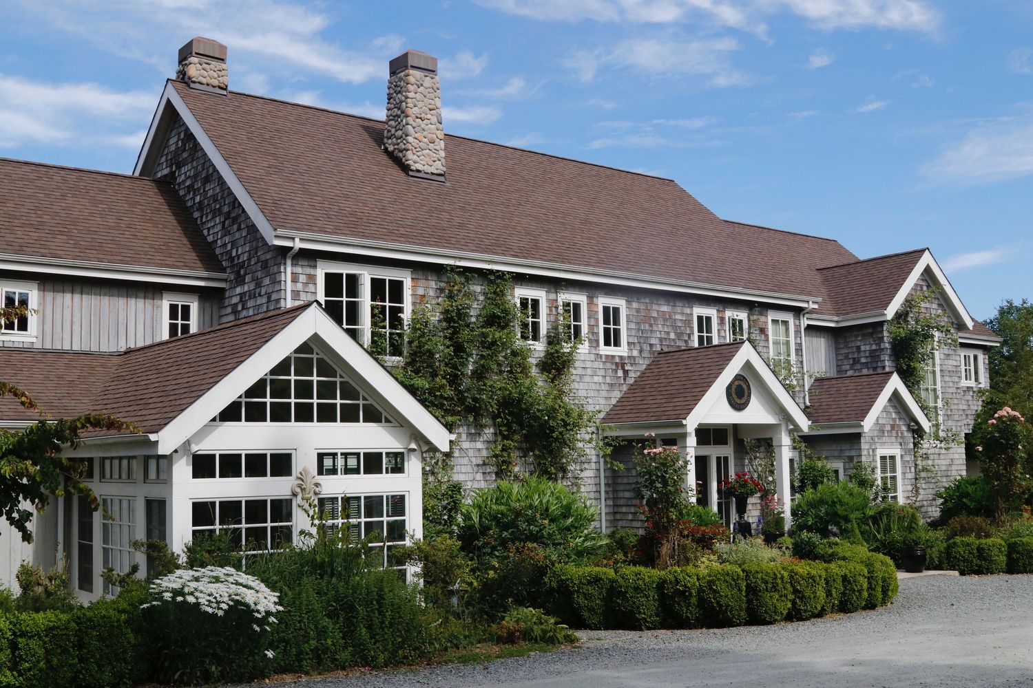 Charming gray shingle-style home with white trim, climbing vines, and manicured landscaping.