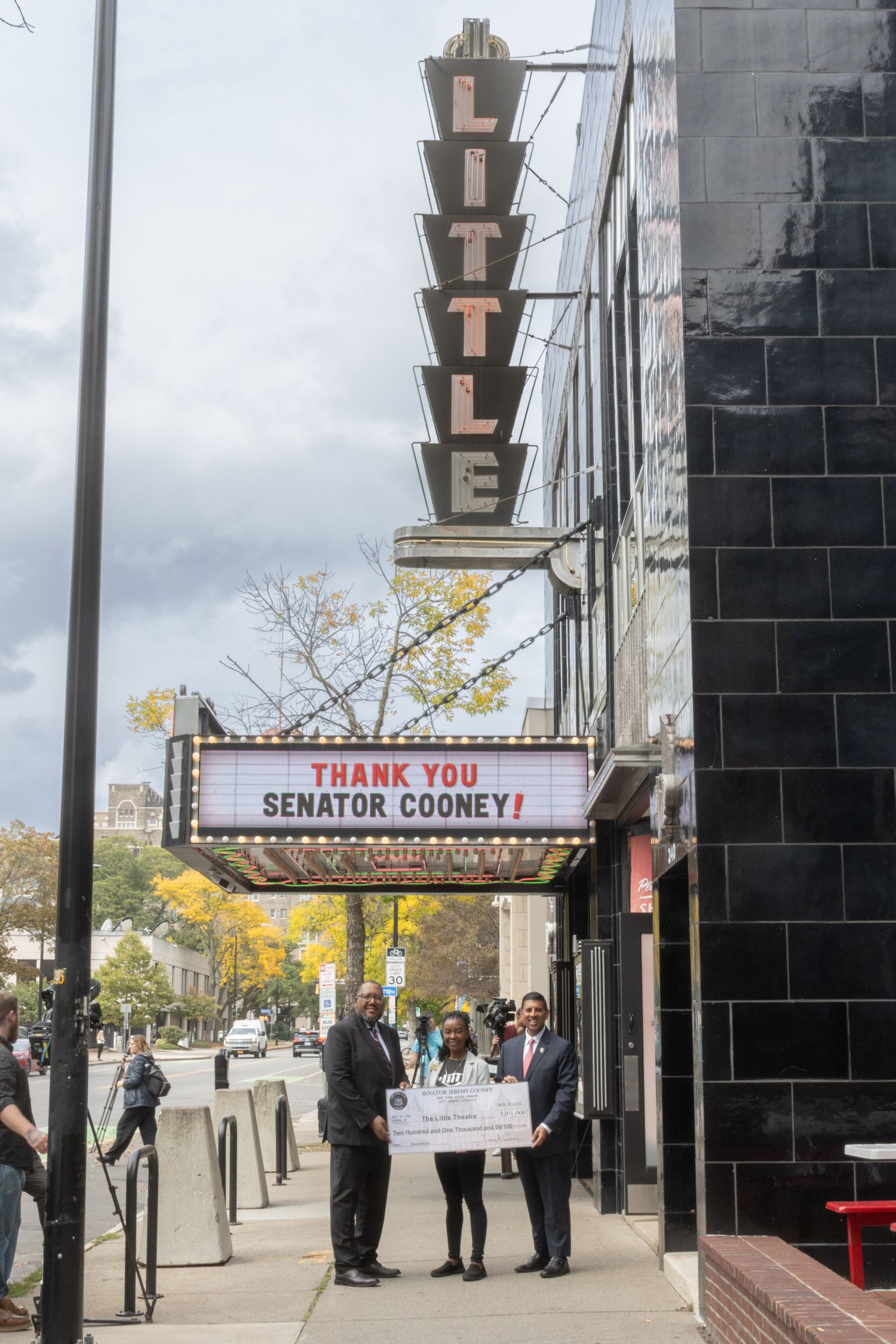 People hold oversized check outside Little Theatre marquee thanking Senator Cooney.