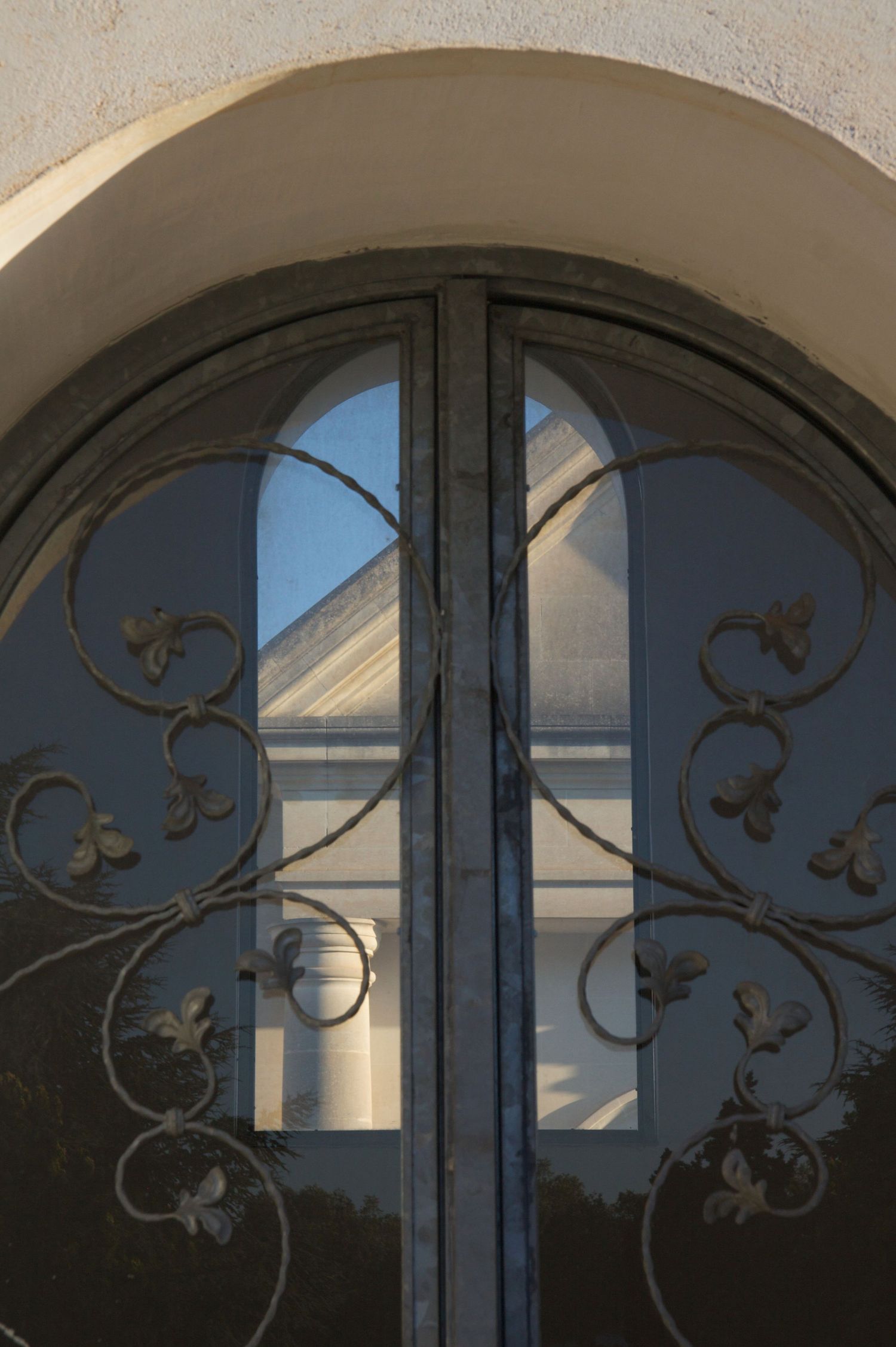 Ornate wrought iron double doors with floral scrollwork set in a round arch, reflecting a classical building with columns.
