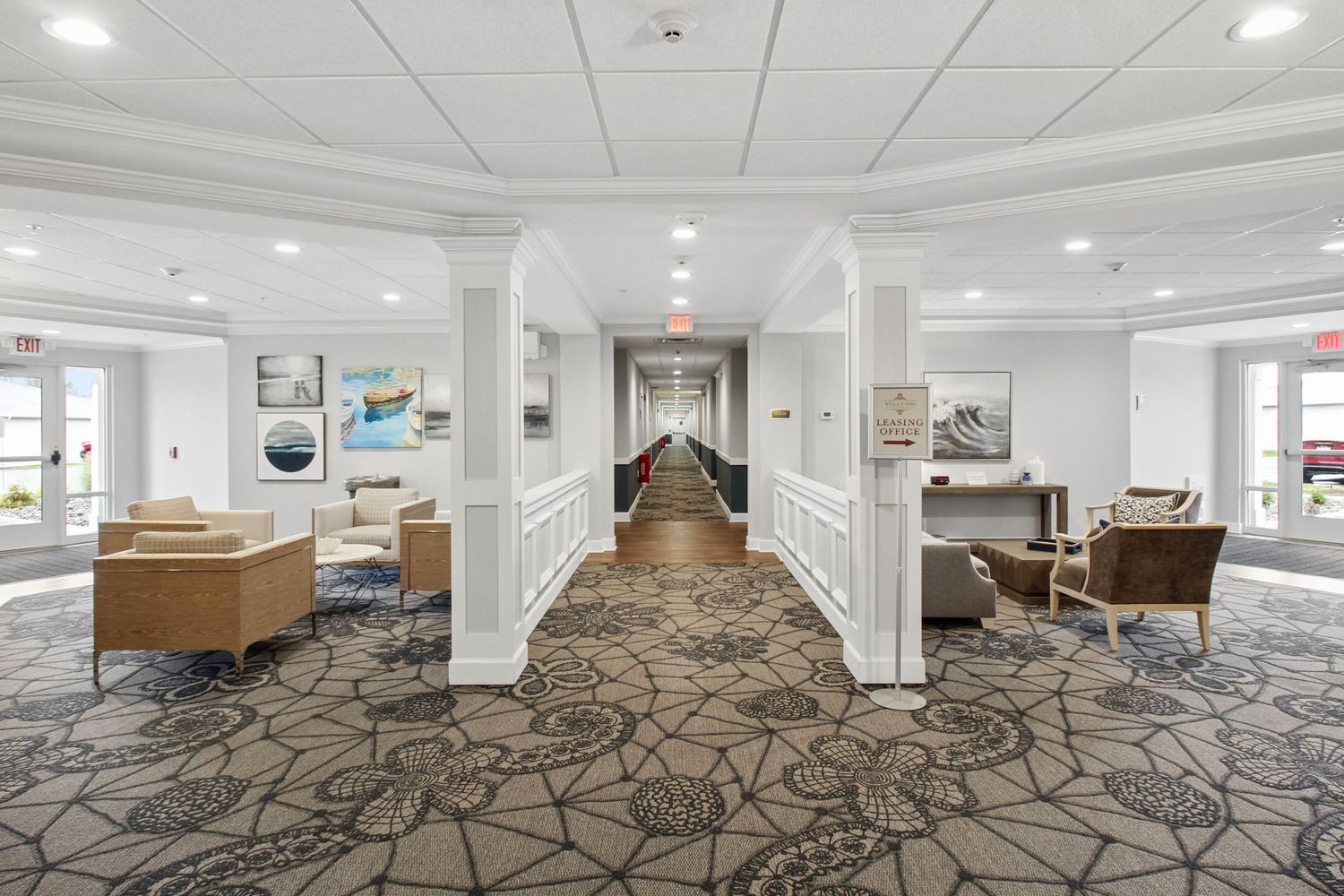 Elegant senior living community hallway with white columns, patterned carpet, and comfortable seating areas.