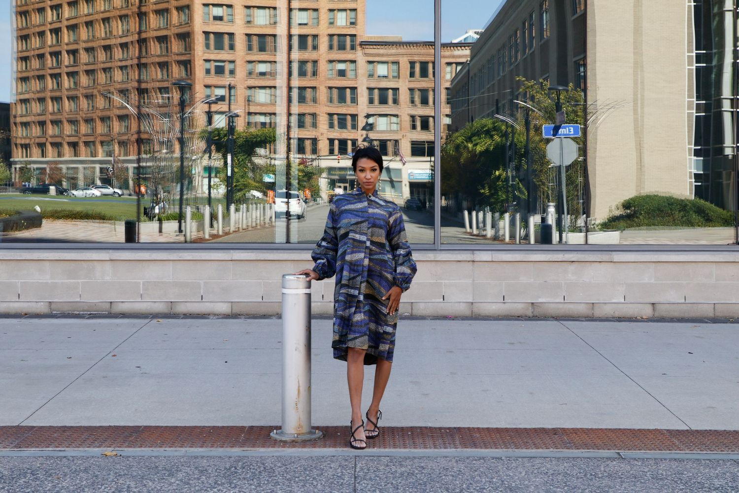Person in boutique outfit standing on urban sidewalk with city buildings behind.