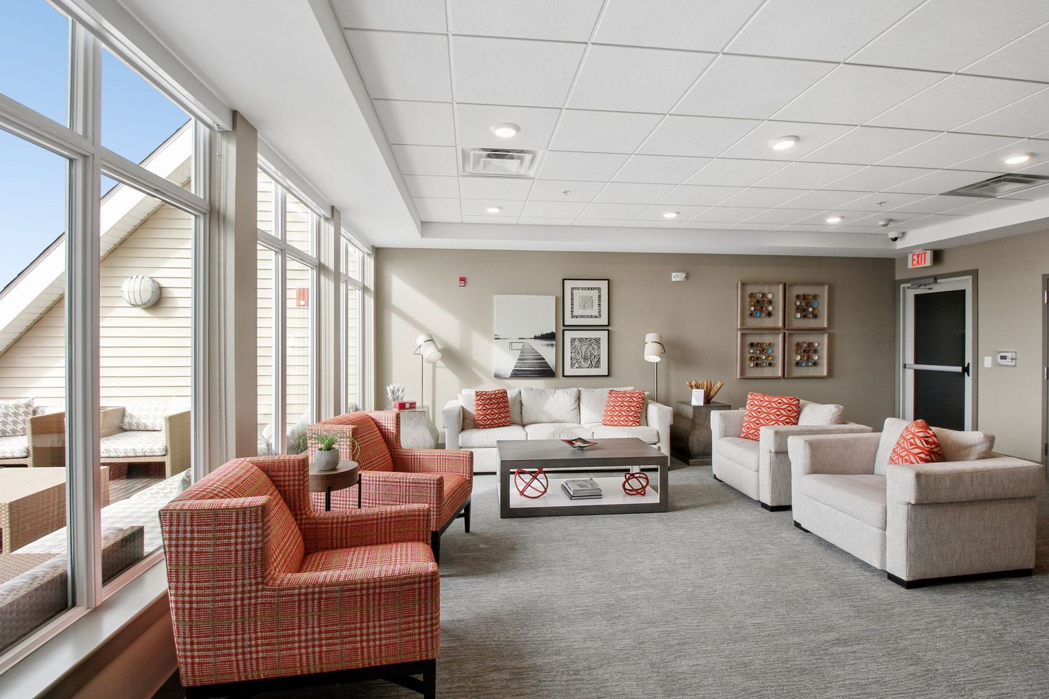 Comfortable apartment community lounge with coral patterned chairs, white sofas, and large floor-to-ceiling windows.