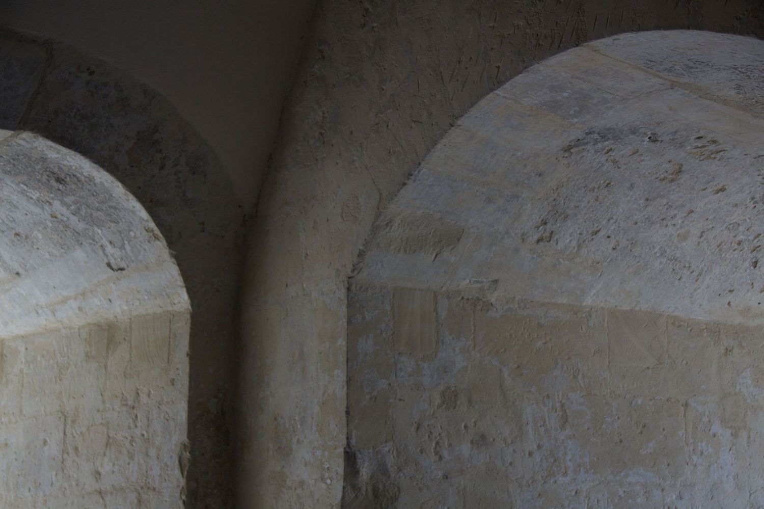 Ancient stone interior with two rounded arches creating dramatic shadows in historic vaulted space.