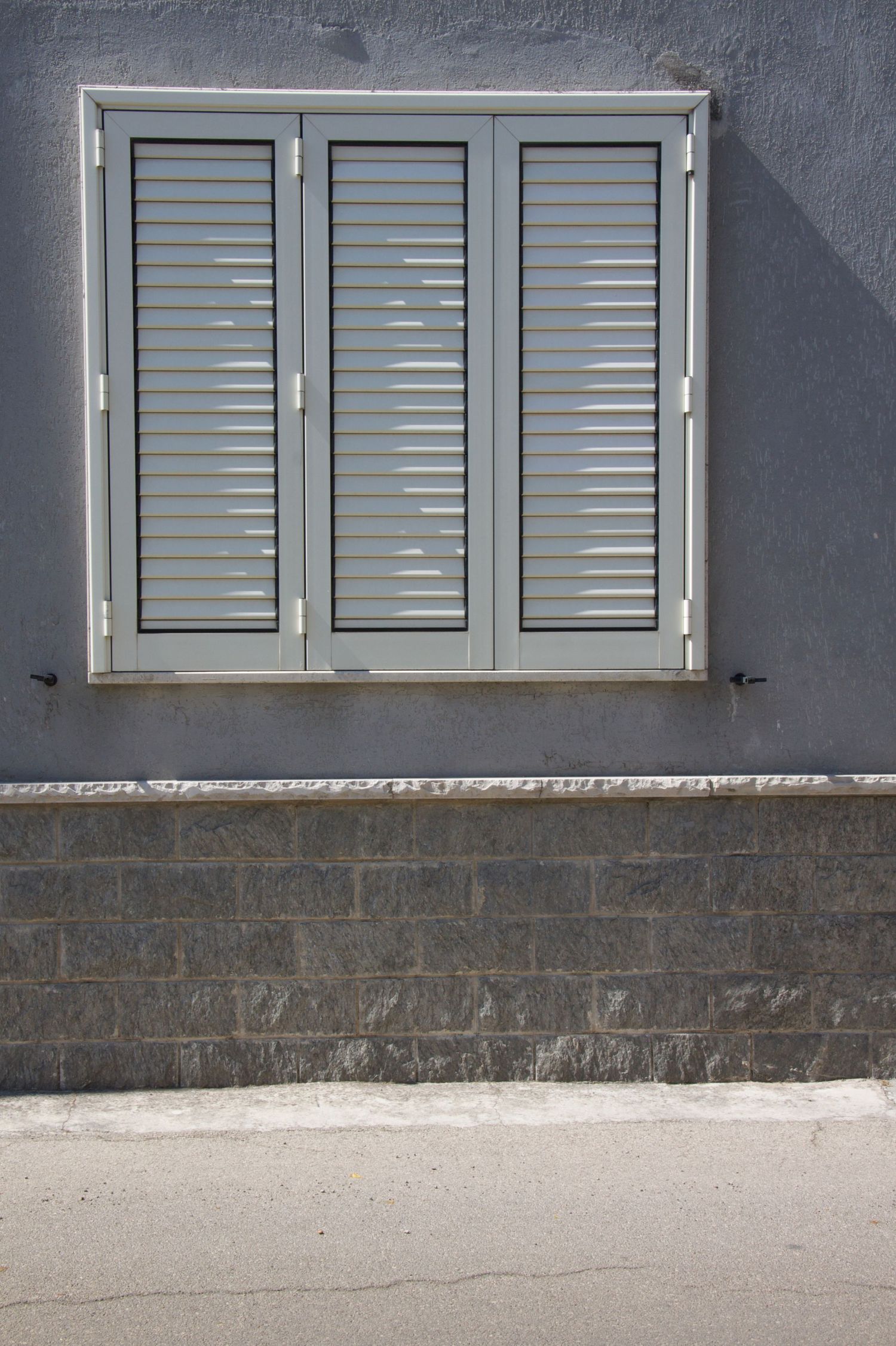Gray shuttered window on a gray plastered wall above a stone base.