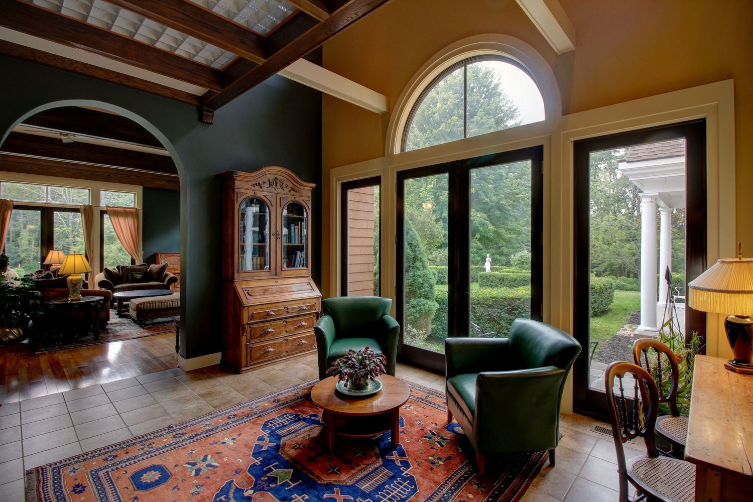 Elegant living room with arched windows, green armchairs, and colorful Persian rug.