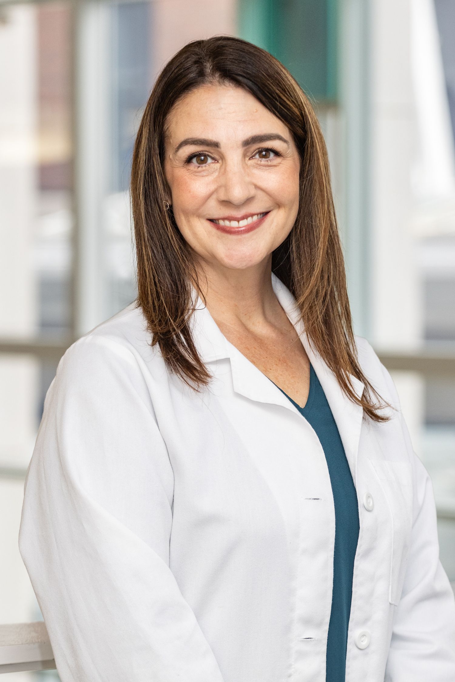 Female doctor in white lab coat smiling in bright modern medical facility.