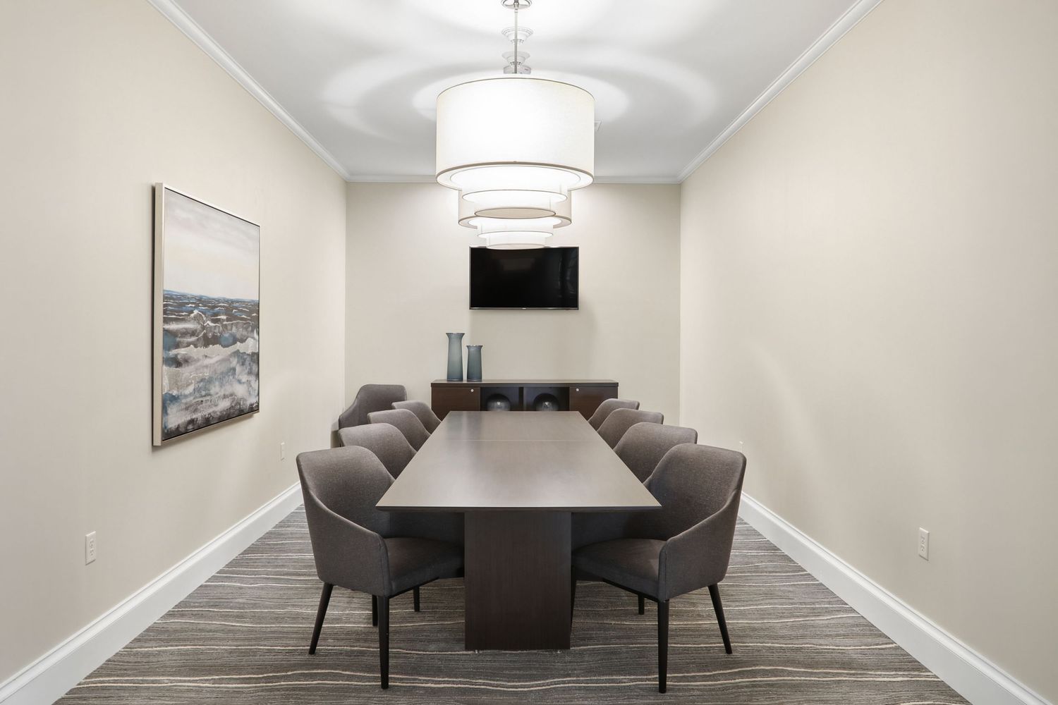 Elegant conference room with long wooden table, gray chairs, pendant light, and wall-mounted TV.