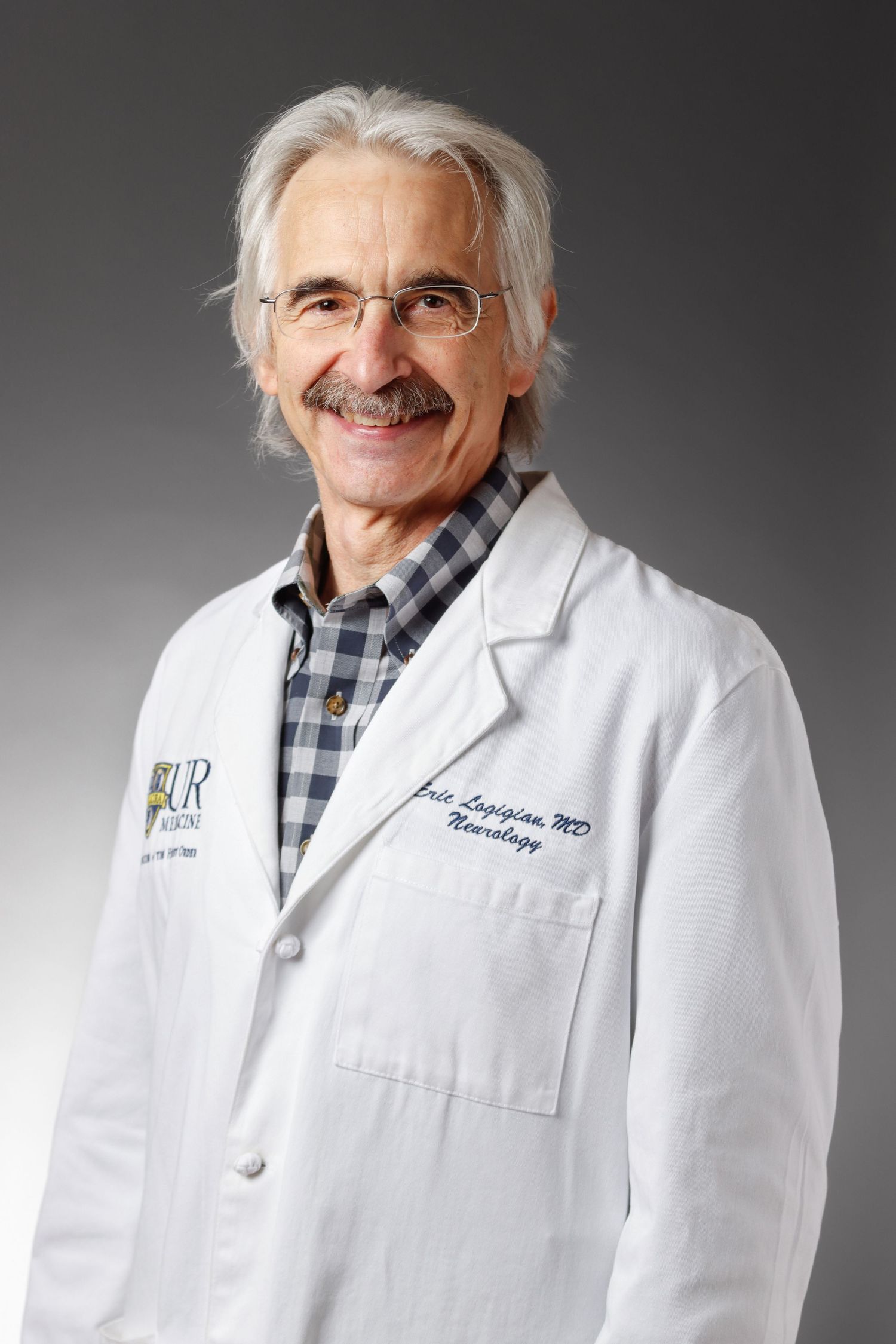 Senior male doctor in white lab coat smiling in professional medical portrait.