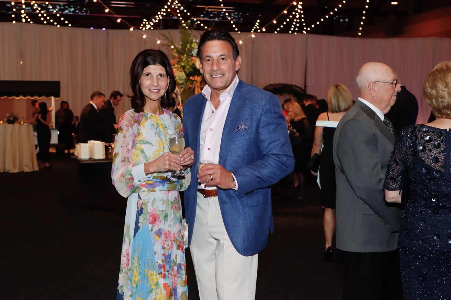 Smiling couple in formal attire enjoying drinks at an elegant indoor gala event.