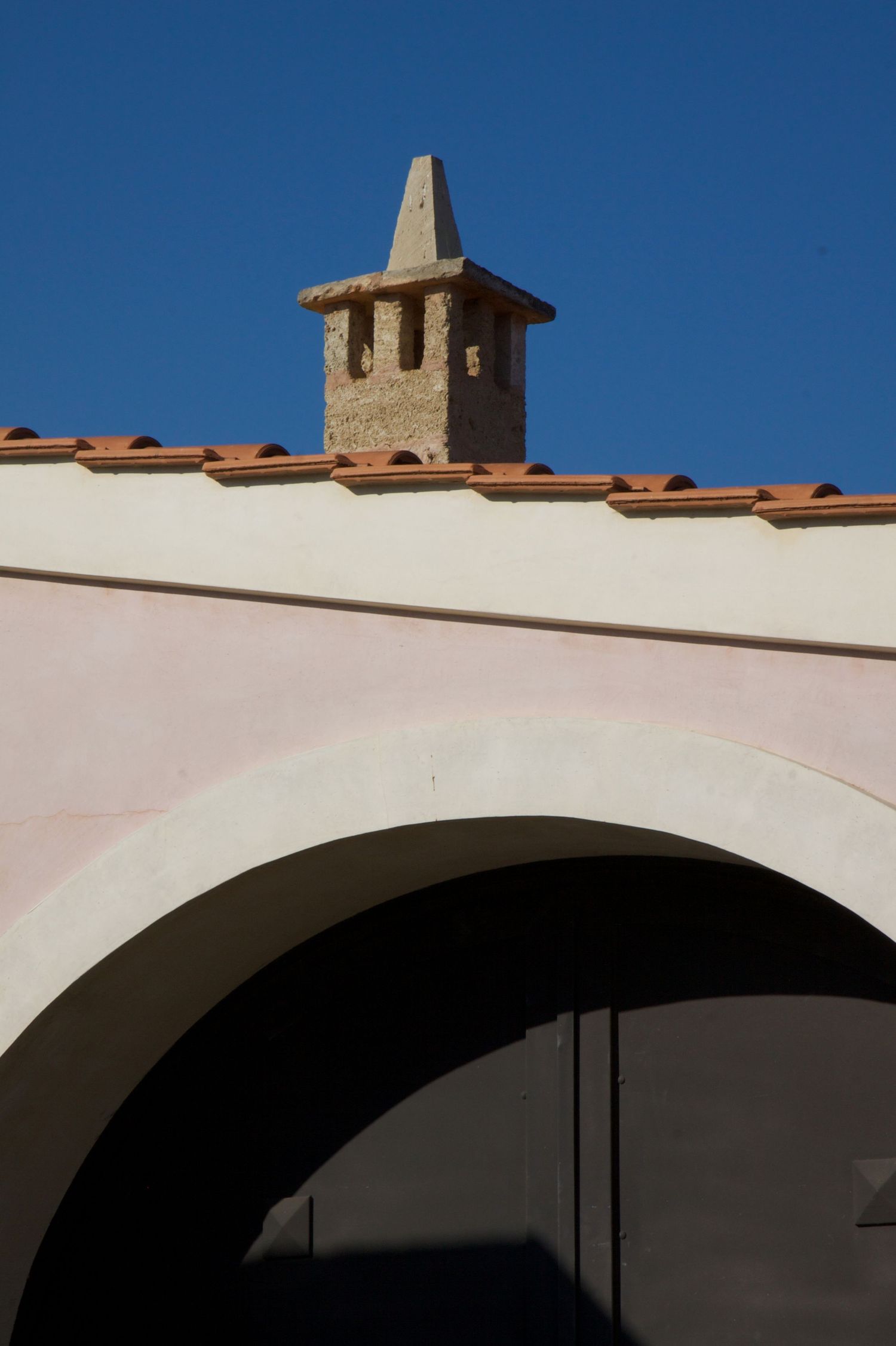 Pink stucco building with white arch and traditional stone chimney against a clear blue sky.