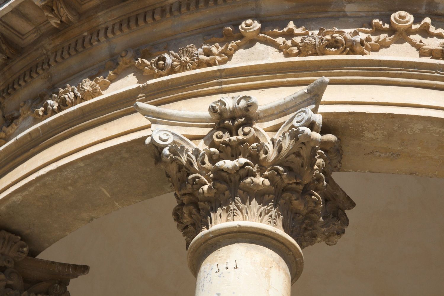 Elaborate Baroque stone column capital with acanthus leaf carvings beneath a decorative arch on a classical building.