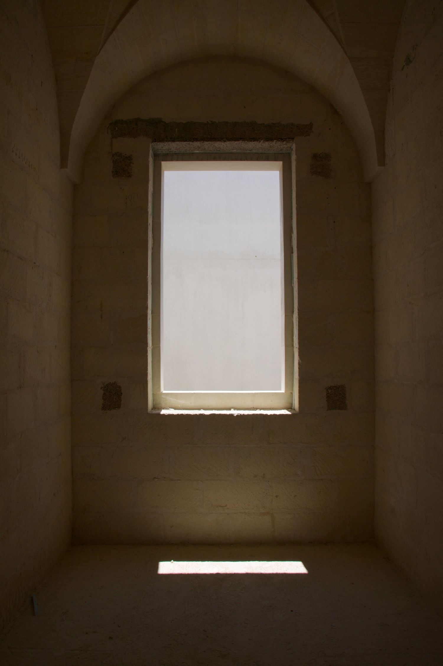 Dark stone interior room with arched ceiling and bright rectangular window casting light on floor.
