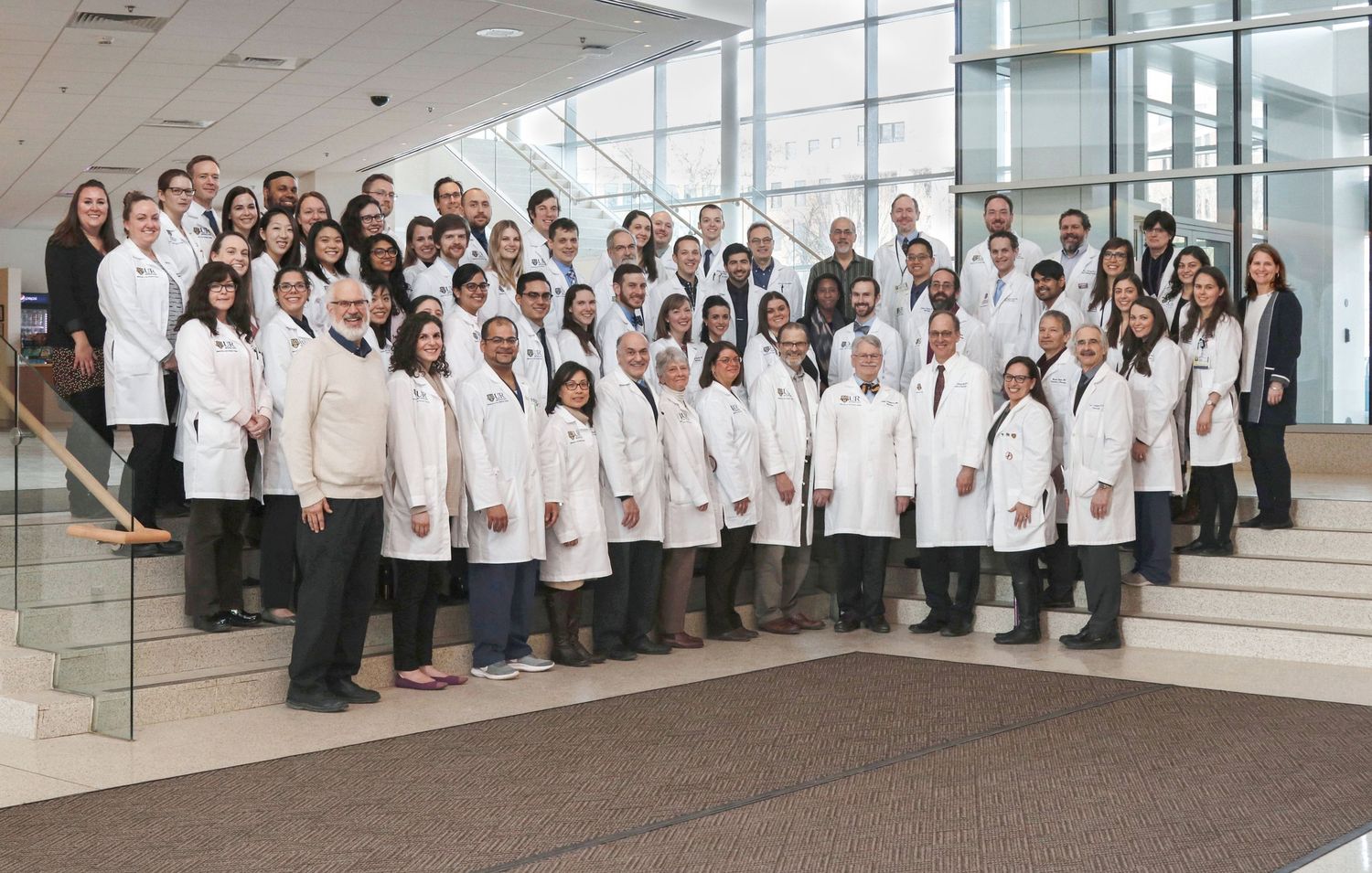 Large group of healthcare staff in white coats posing together in a bright modern medical facility.