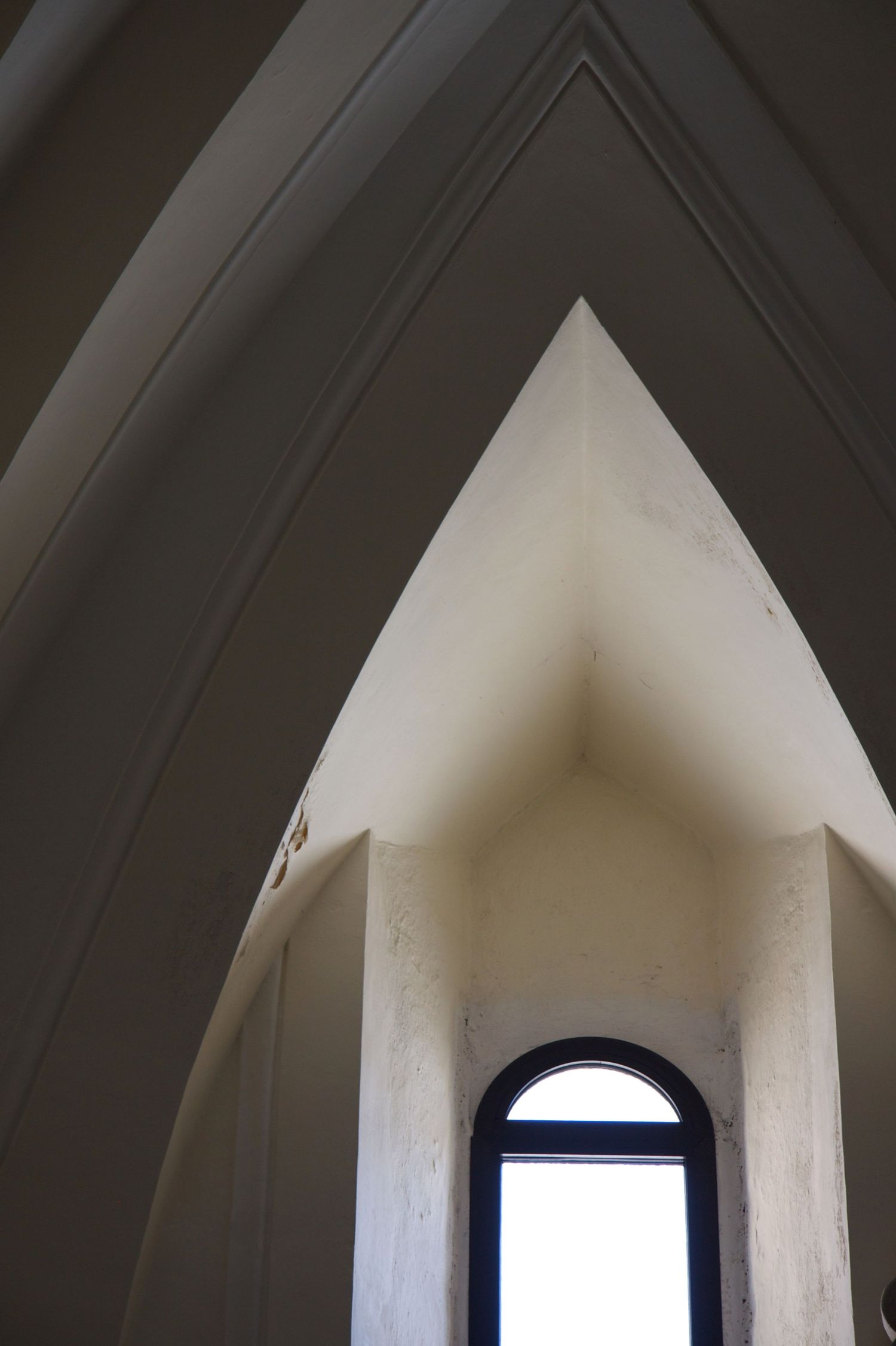 Gothic pointed arch interior ceiling converging toward a small arched window with bright light in a stone building.