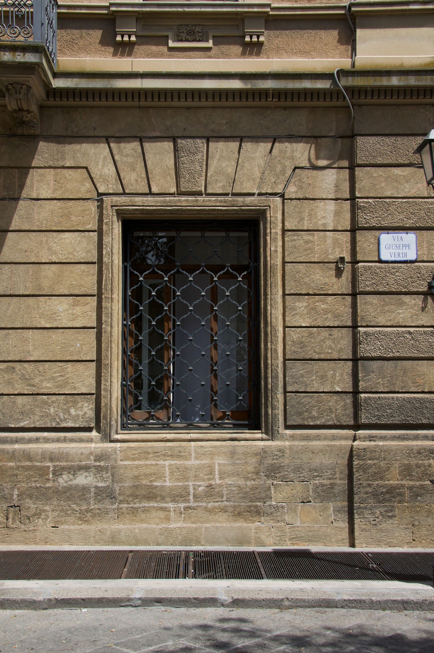Historic stone building facade with ornate framed window covered by decorative iron lattice grille.