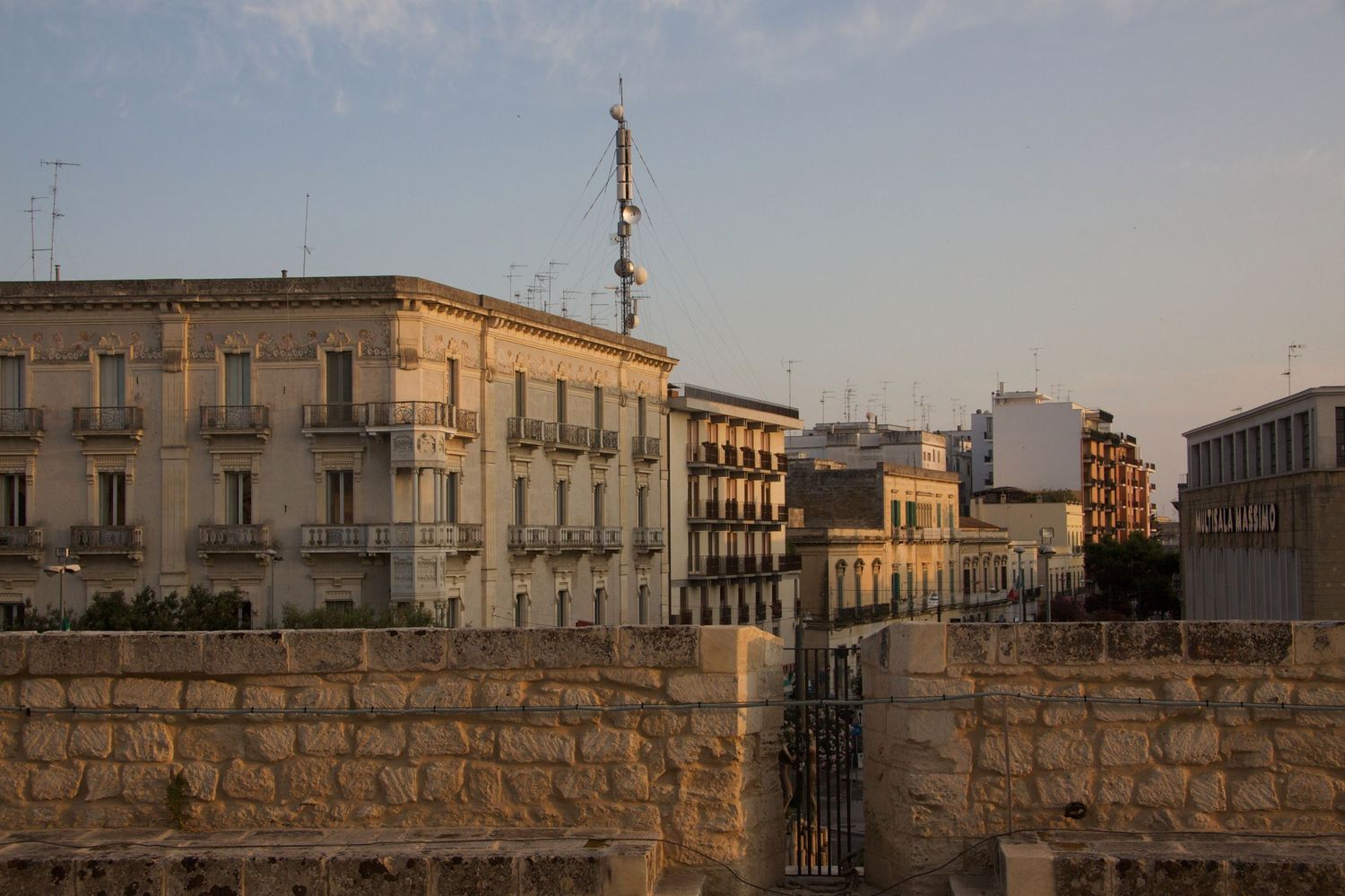Historic European city buildings with balconies and ancient stone walls bathed in warm golden sunset light.