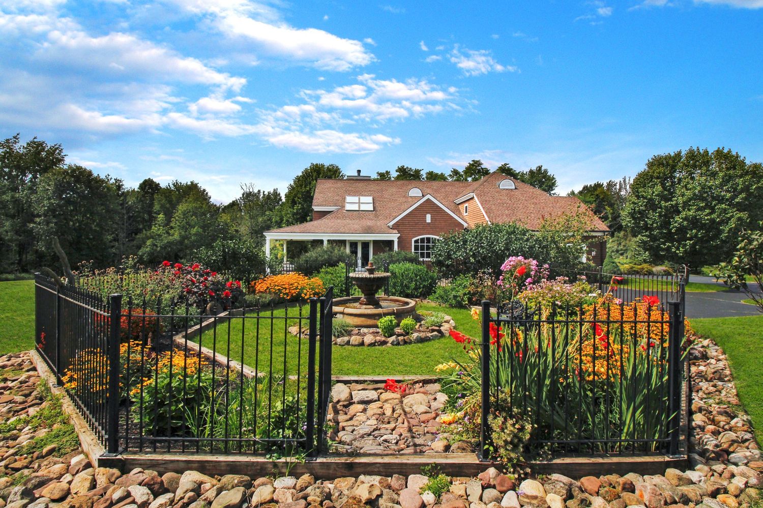 Brick ranch home with ornate iron fence, stone garden, and colorful flower beds.