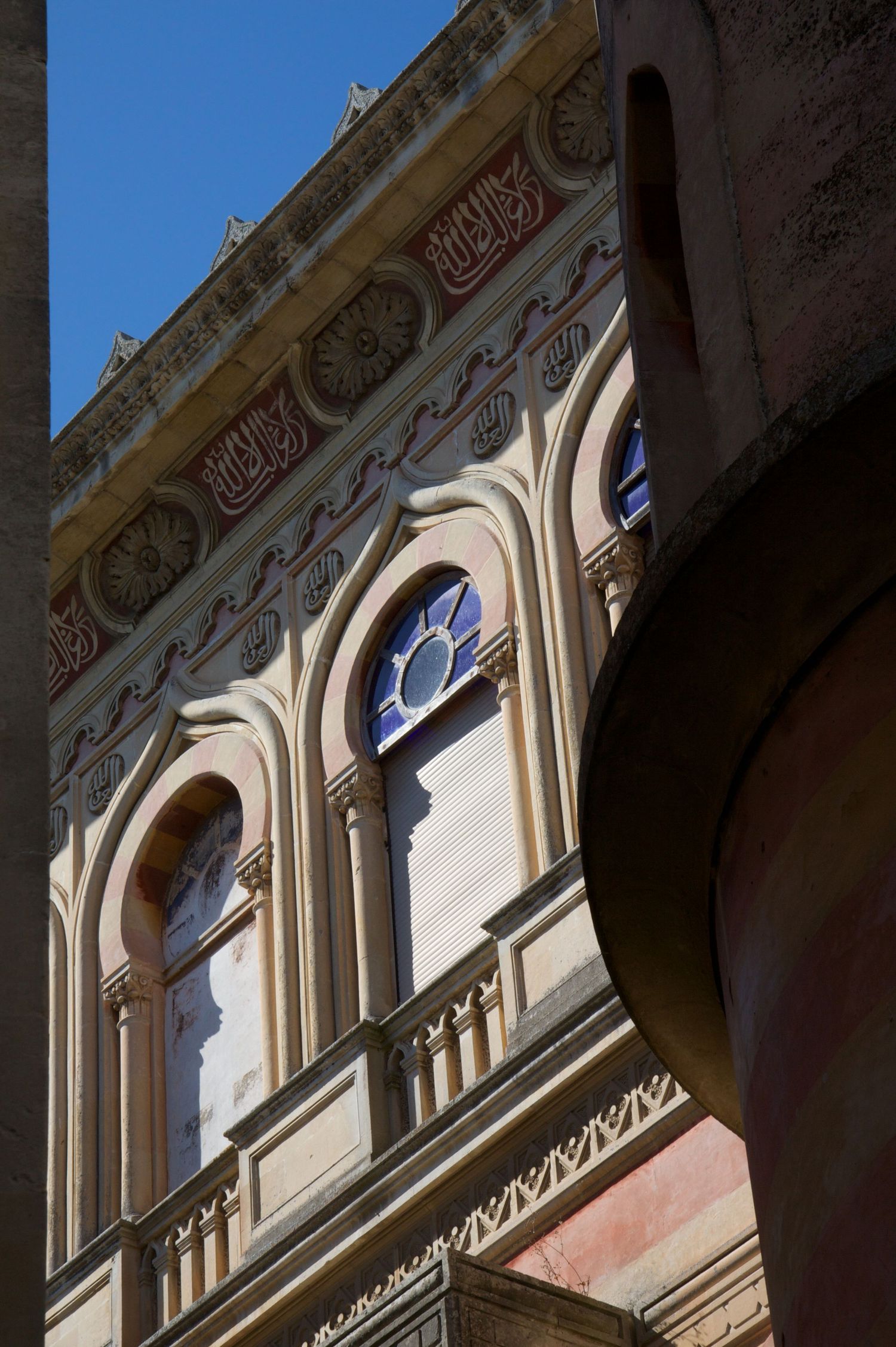 Ornate facade of a historic building with arched windows and decorative Islamic calligraphy.