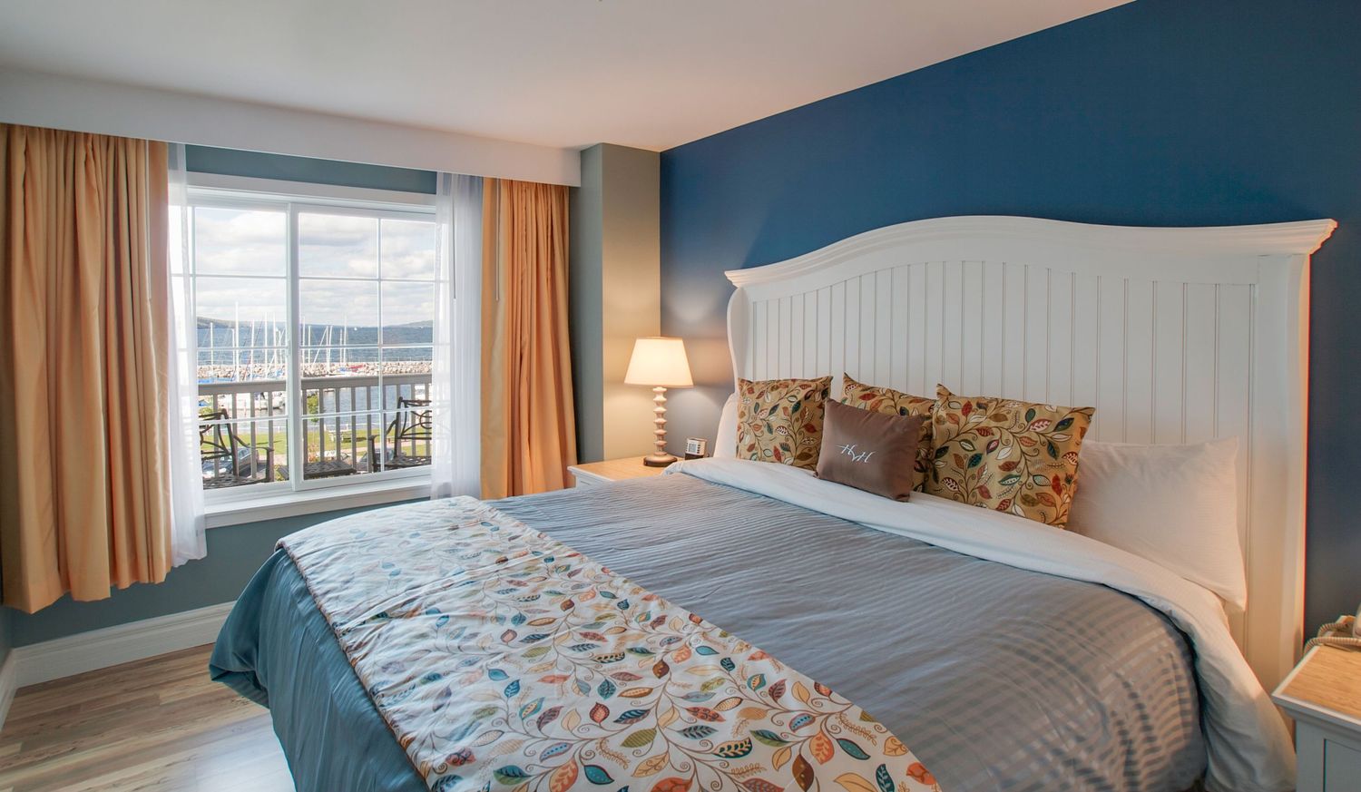 Bright hotel bedroom with king bed, blue accent wall, and scenic waterfront window view.