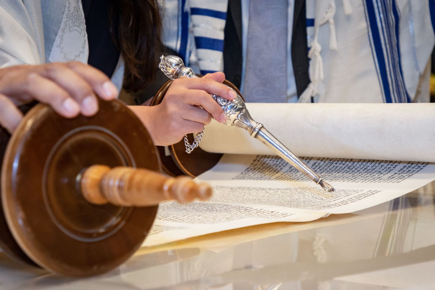 Close-up of hands holding a Torah pointer while reading from a Hebrew scroll during a Jewish ceremony.